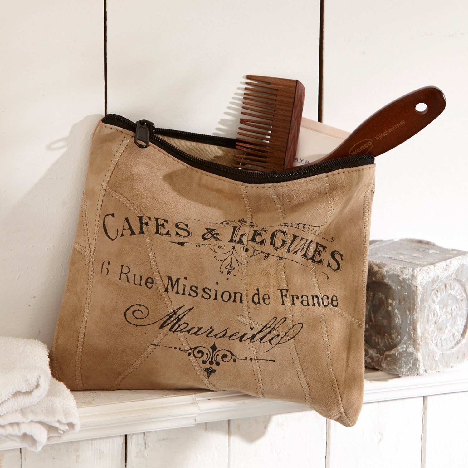 Tasje Jeannice Beige suède make-uptasje met zwarte rits en Franse opdruk, houten kam zichtbaar op plank