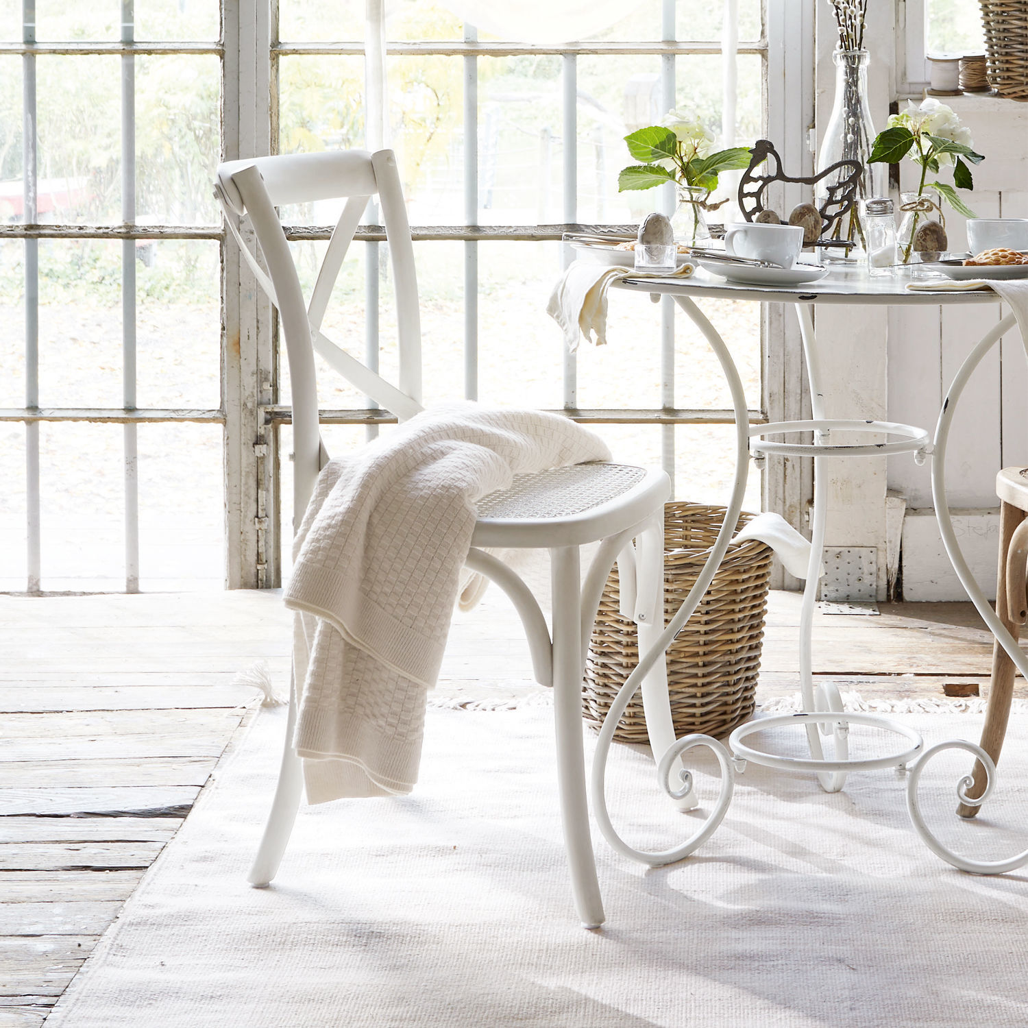 Witte houten stoel met X-vormige rugleuning en gevlochten zitting, crème deken erop in lichte kamer