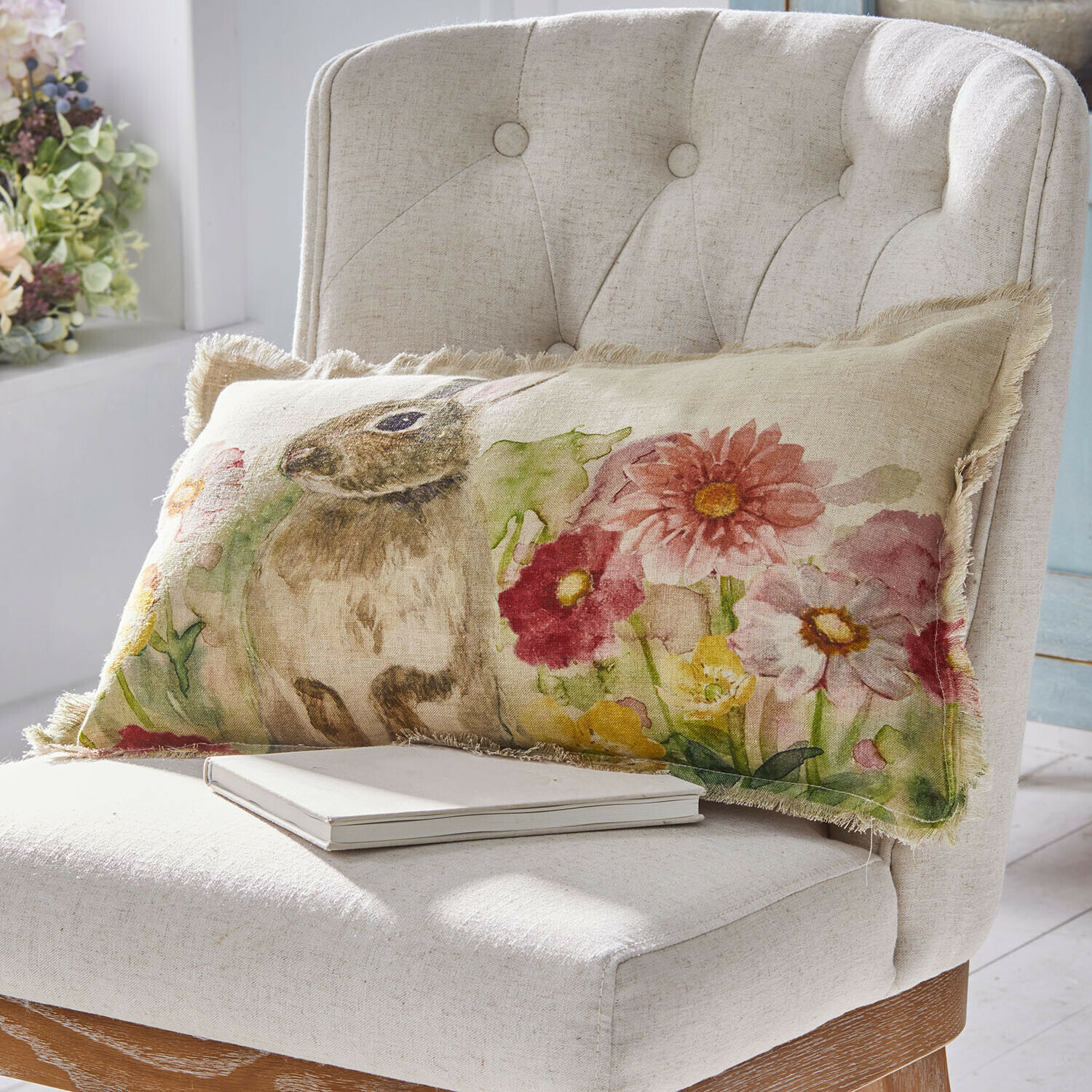 Lang linnen kussen met konijn- en bloemenprint in pasteltinten op lichte stoel