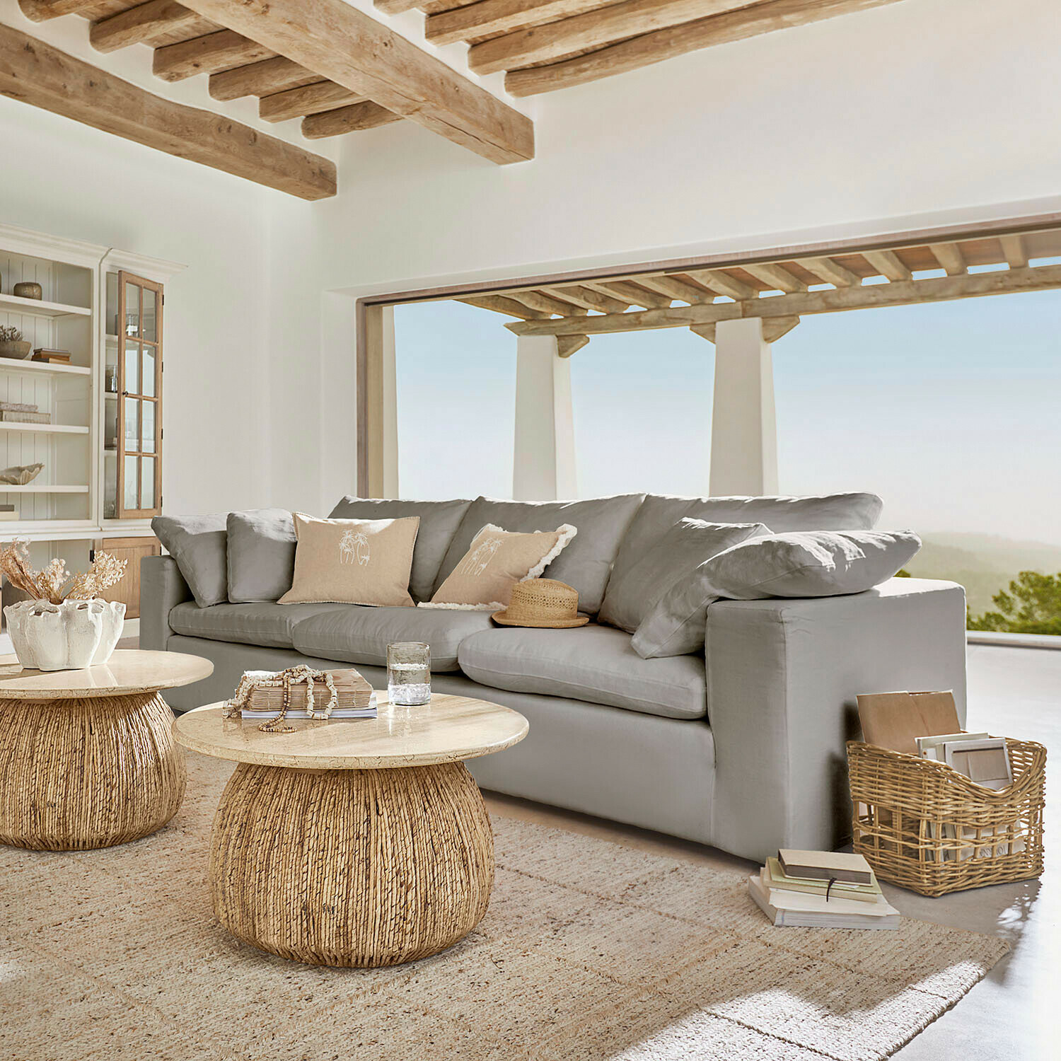 Grijze bank met zachte kussens en natuurlijke houten salontafels in lichte woonkamer met uitzicht