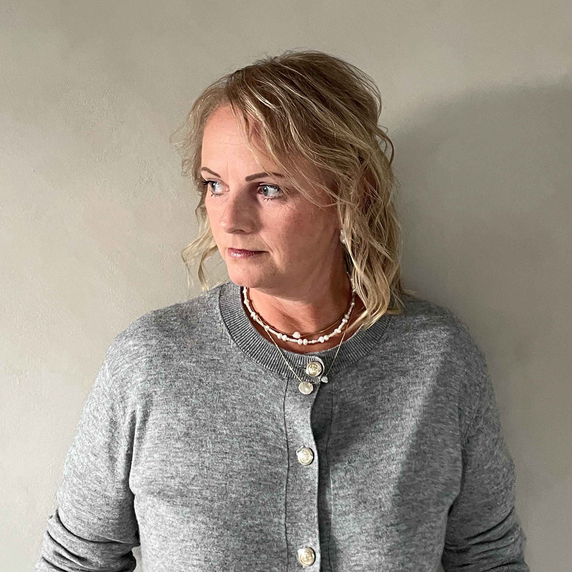 Vrouw in grijze trui met knopen en kettingen, casual stijl tegen lichte achtergrond