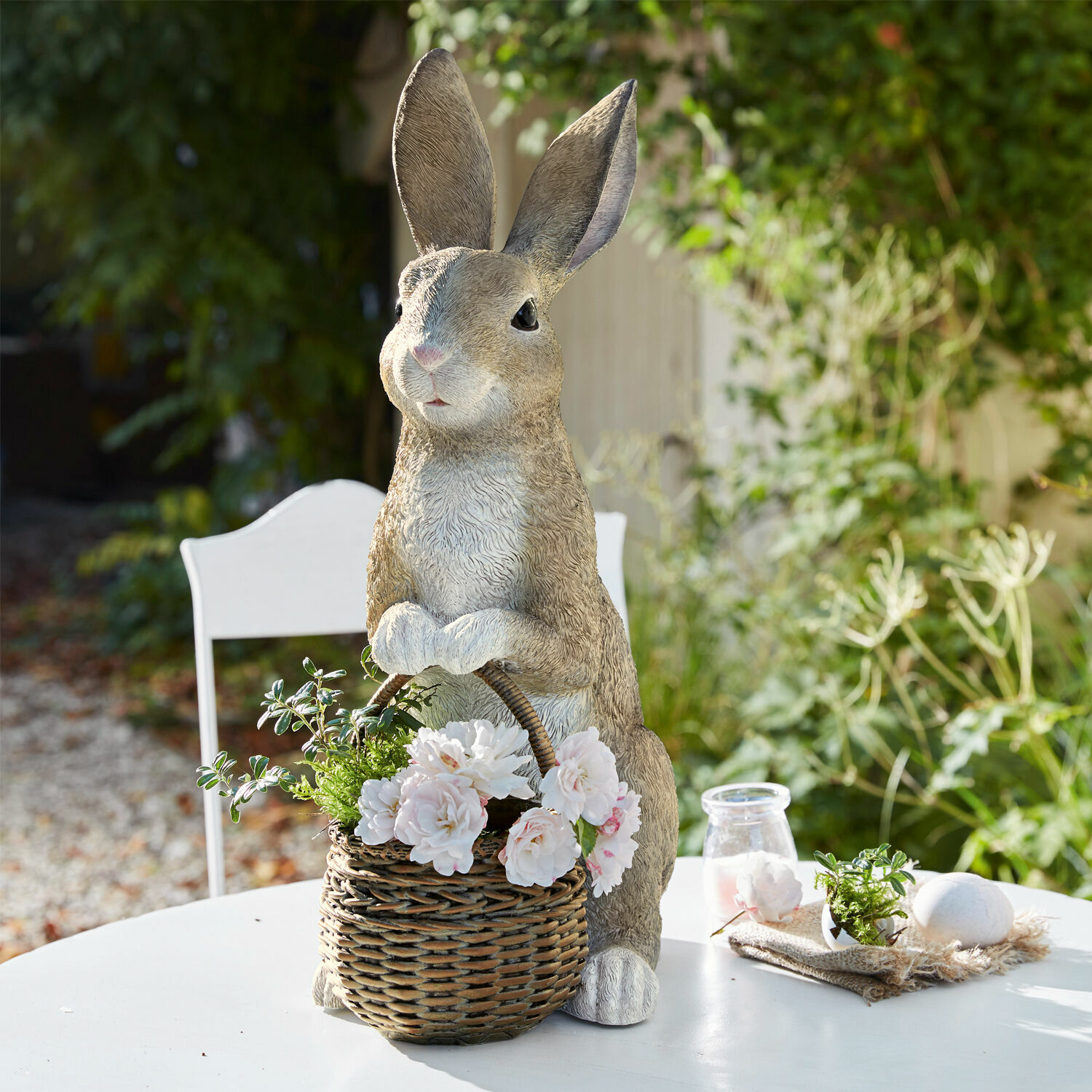 Decoratief konijn van kunststof met rieten mand en witte bloemen op buitentafel