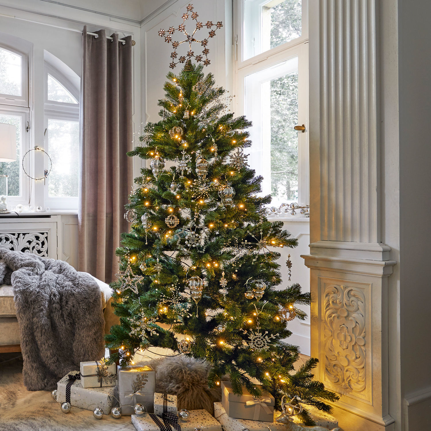 Kerstversiering-set Bjouterie Kerstboom met groene takken en zilveren versieringen in lichte woonkamer met cadeaus eronder