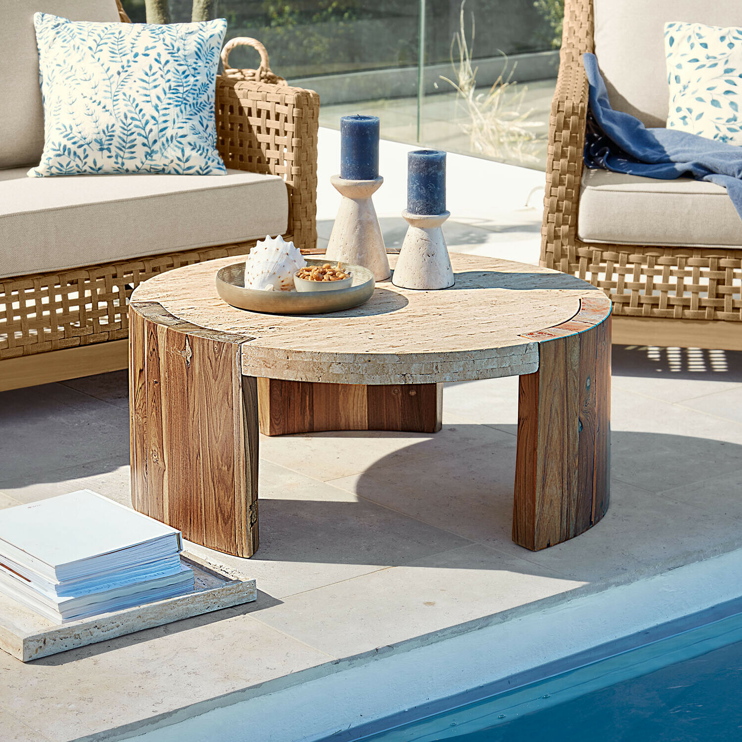 Ronde salontafel van hout en steen op terras bij zwembad met decoratieve kaarsen en schelp