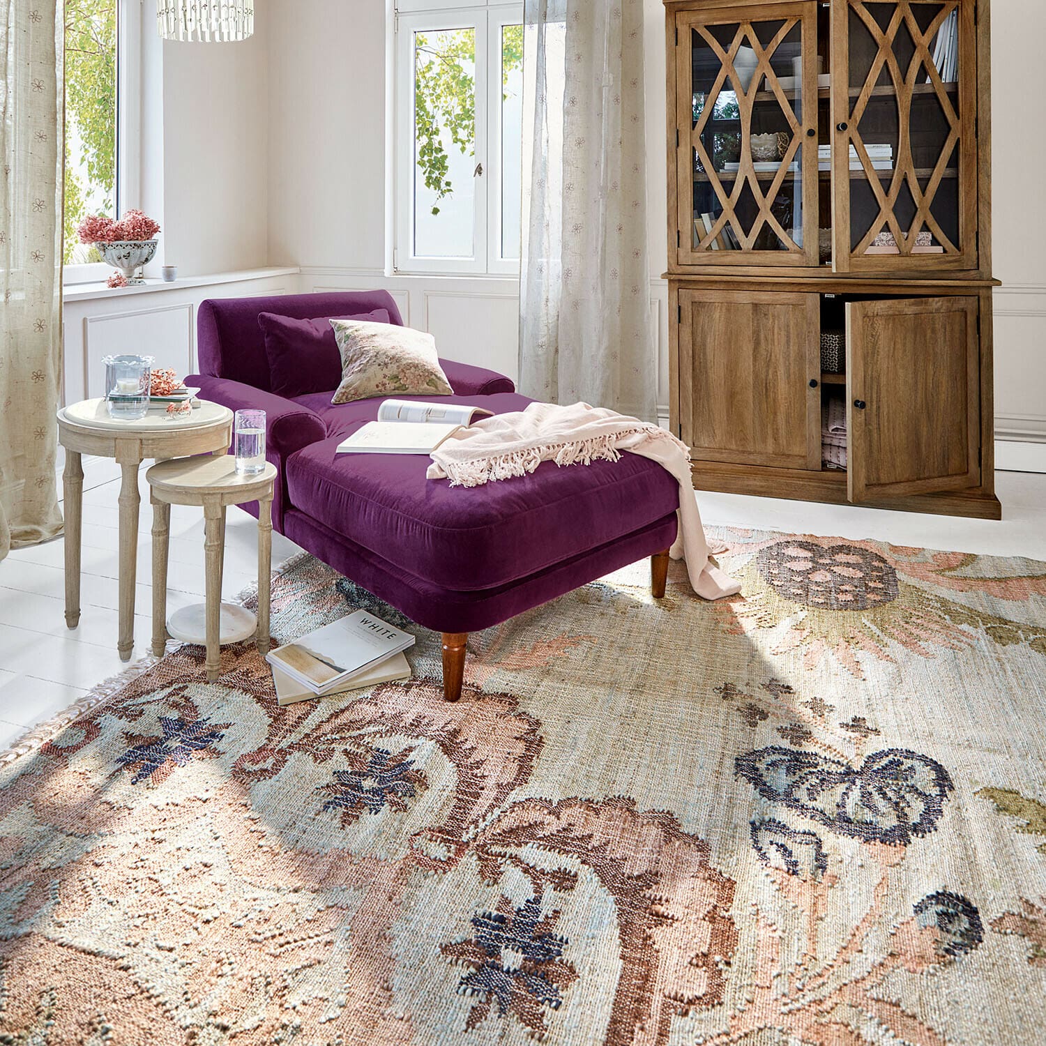 Vloerkleed Amélorie Paars fluwelen ligstoel in lichte woonkamer met houten kast en decoratief vloerkleed