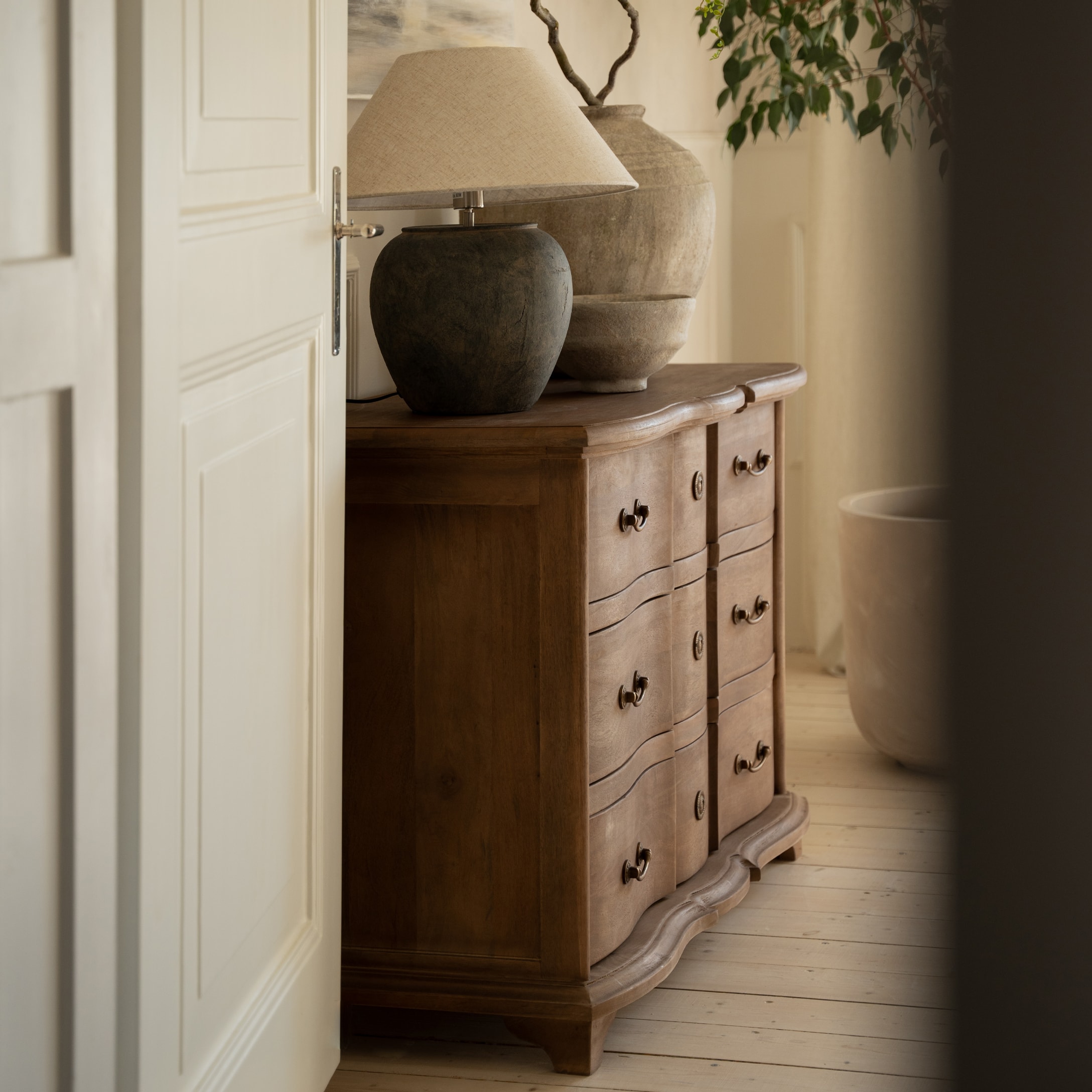 Houten ladekast met decoratieve lades en lamp met beige kap in een gezellige kamer