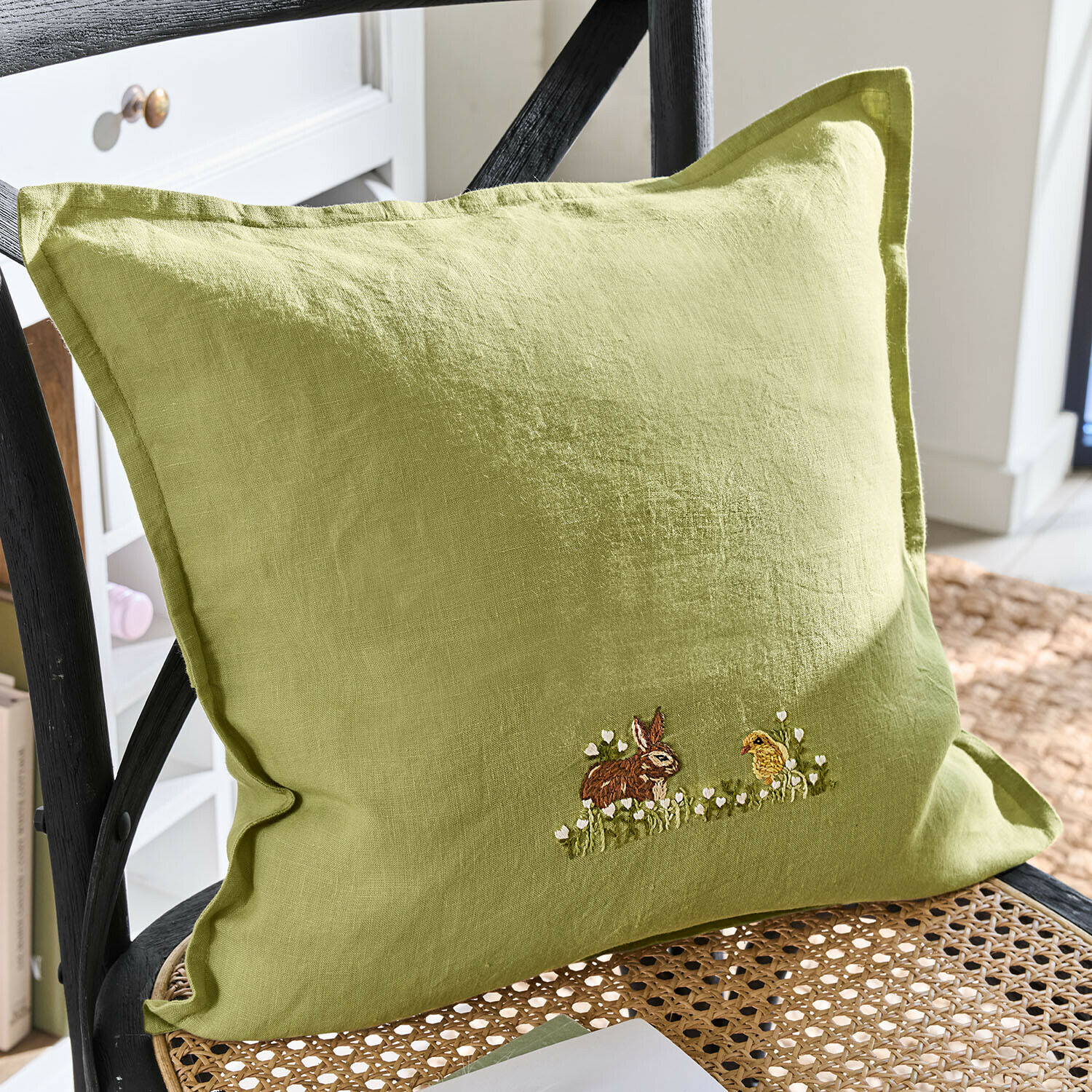 Groen linnen kussen met borduurwerk van konijn en kuiken op gevlochten stoel, woondecoratie