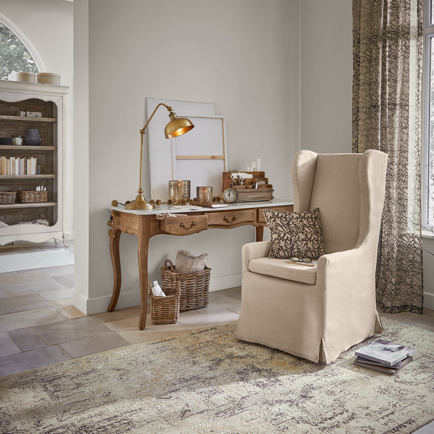 Beige stoffen oorfauteuil in klassieke woonkamer met houten bureau en tafellamp