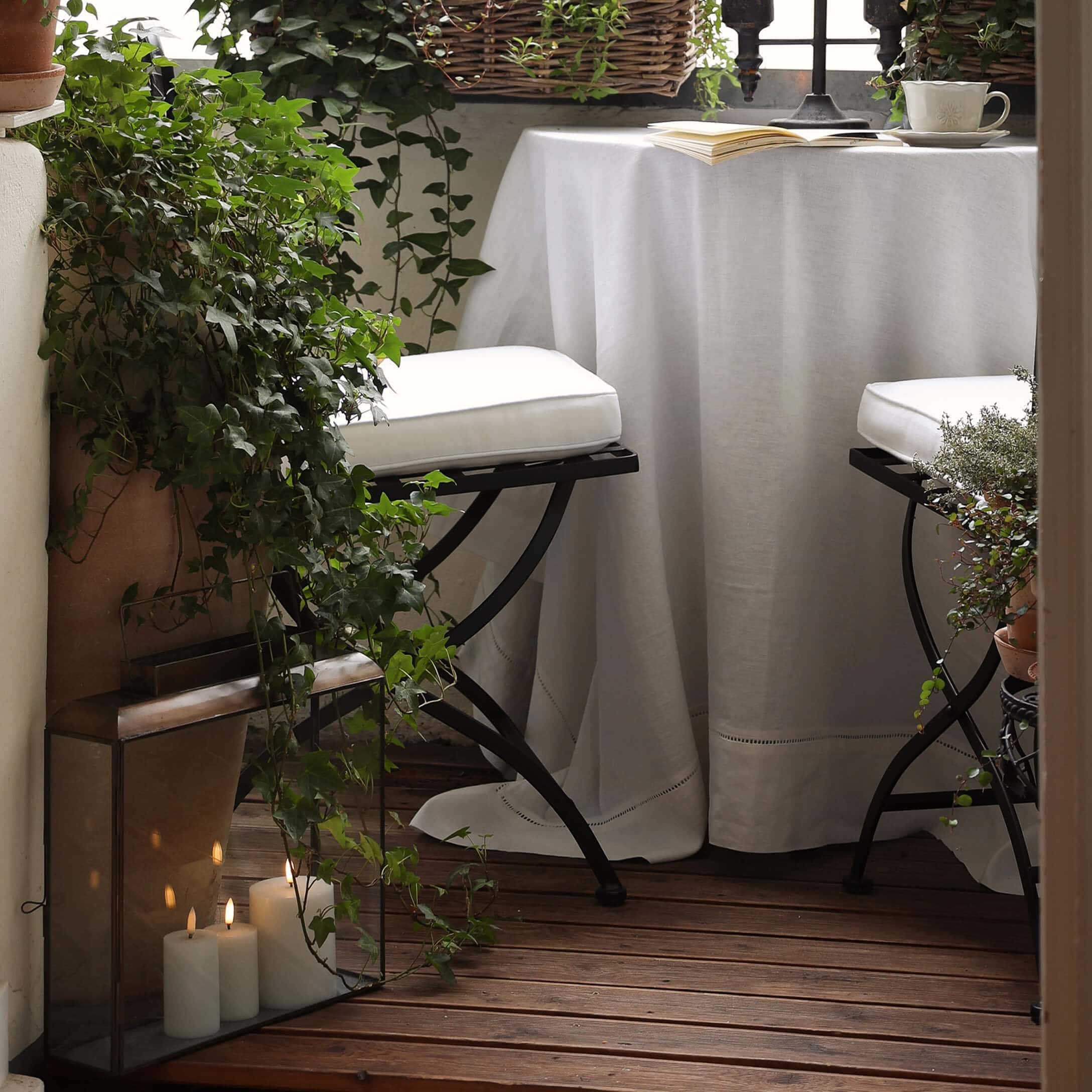Gezellig balkon met houten vloer, wit tafelkleed en metalen stoelen met witte kussens