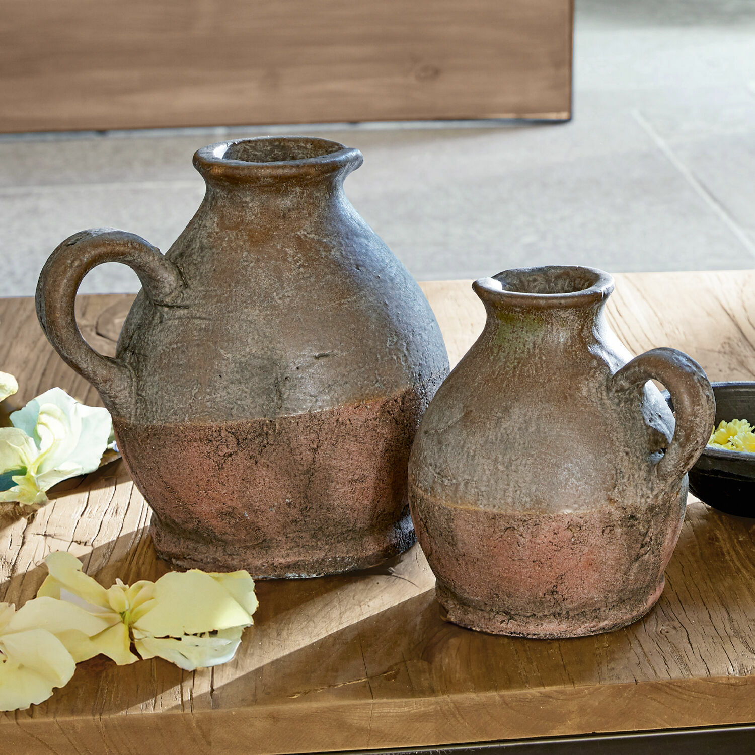 Twee rustieke keramische kruiken in bruin-roestkleur op houten tafel met bloemen