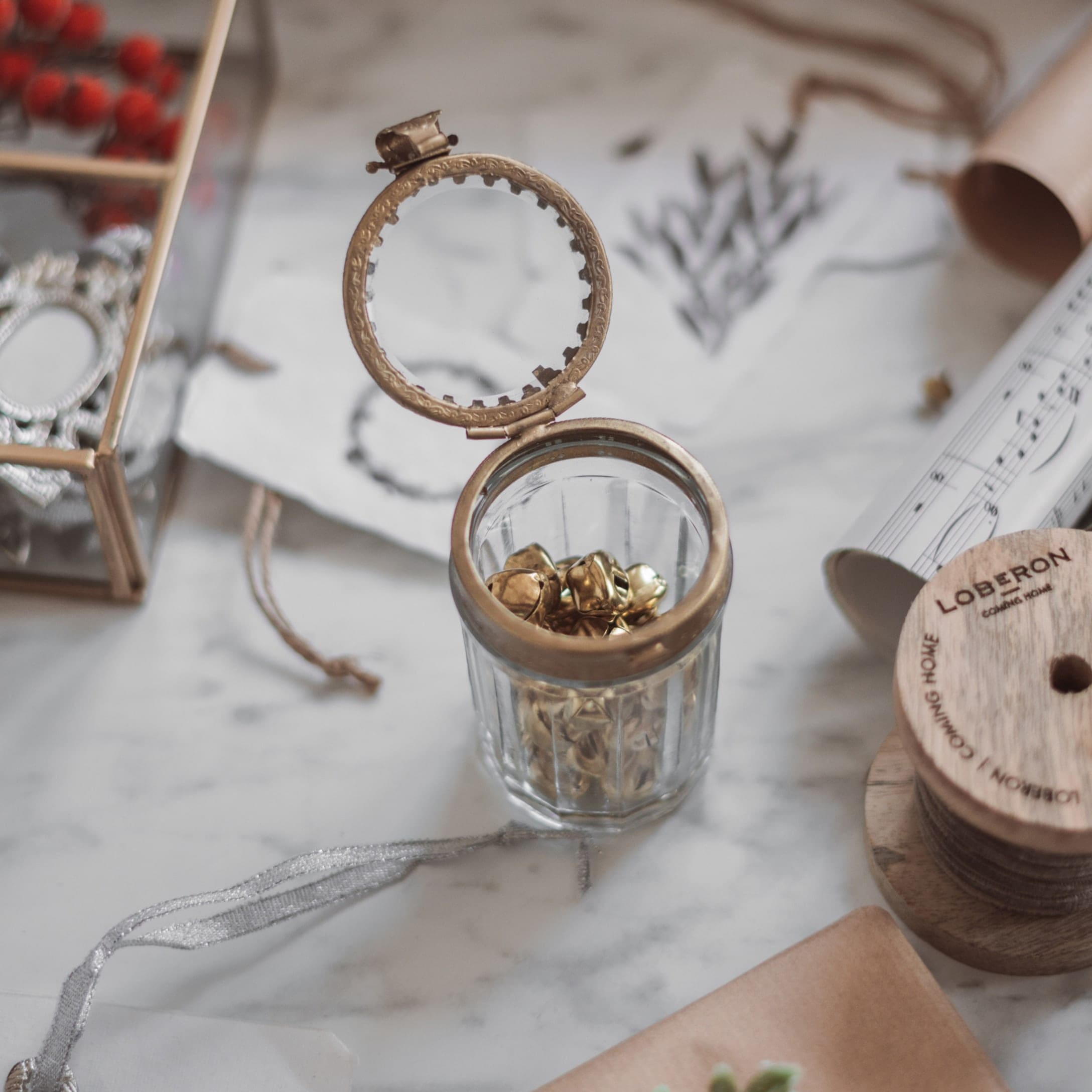 Glazen pot met messing deksel en gouden belletjes op marmeren blad, feestelijke decoratie