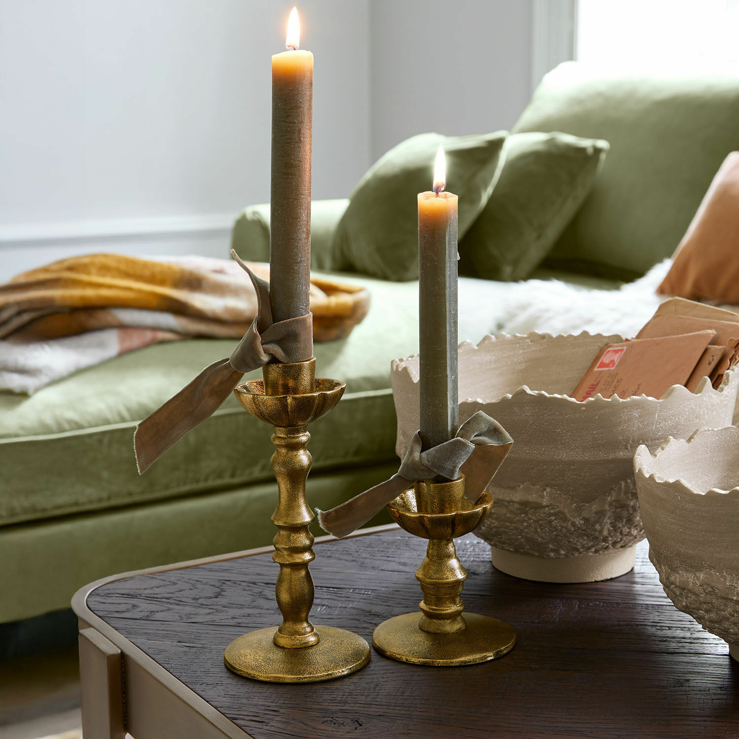 Kandelaar set van 2 Zalethar Set van twee gouden metalen kandelaars met grijze kaarsen en decoratieve linten op houten tafel