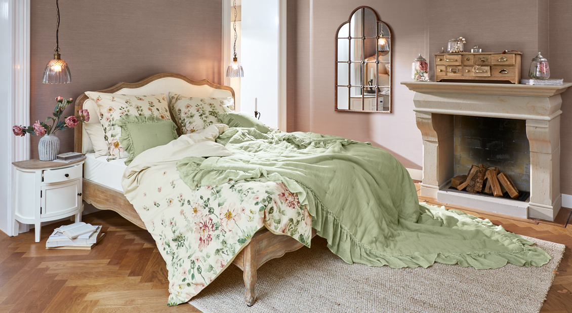 Franse slaapkamer met houten bed, groene katoenen deken en bloemig beddengoed voor een gezellige sfeer