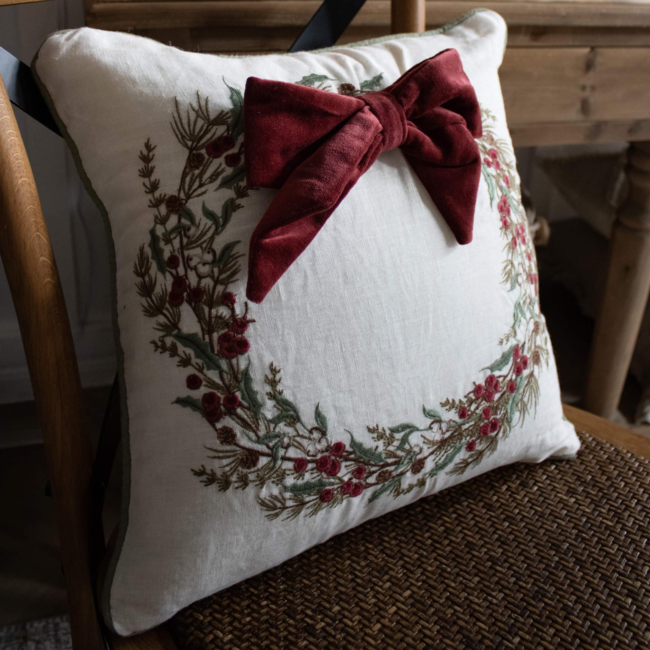 Witte linnen kussen met geborduurde krans en bordeauxrode fluwelen strik, woondecoratie