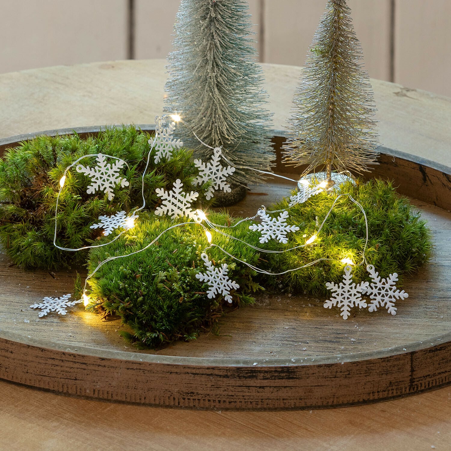 Lichtsnoer Azmira Decoratieve LED-slinger met witte sneeuwvlokken op groen mos op houten dienblad