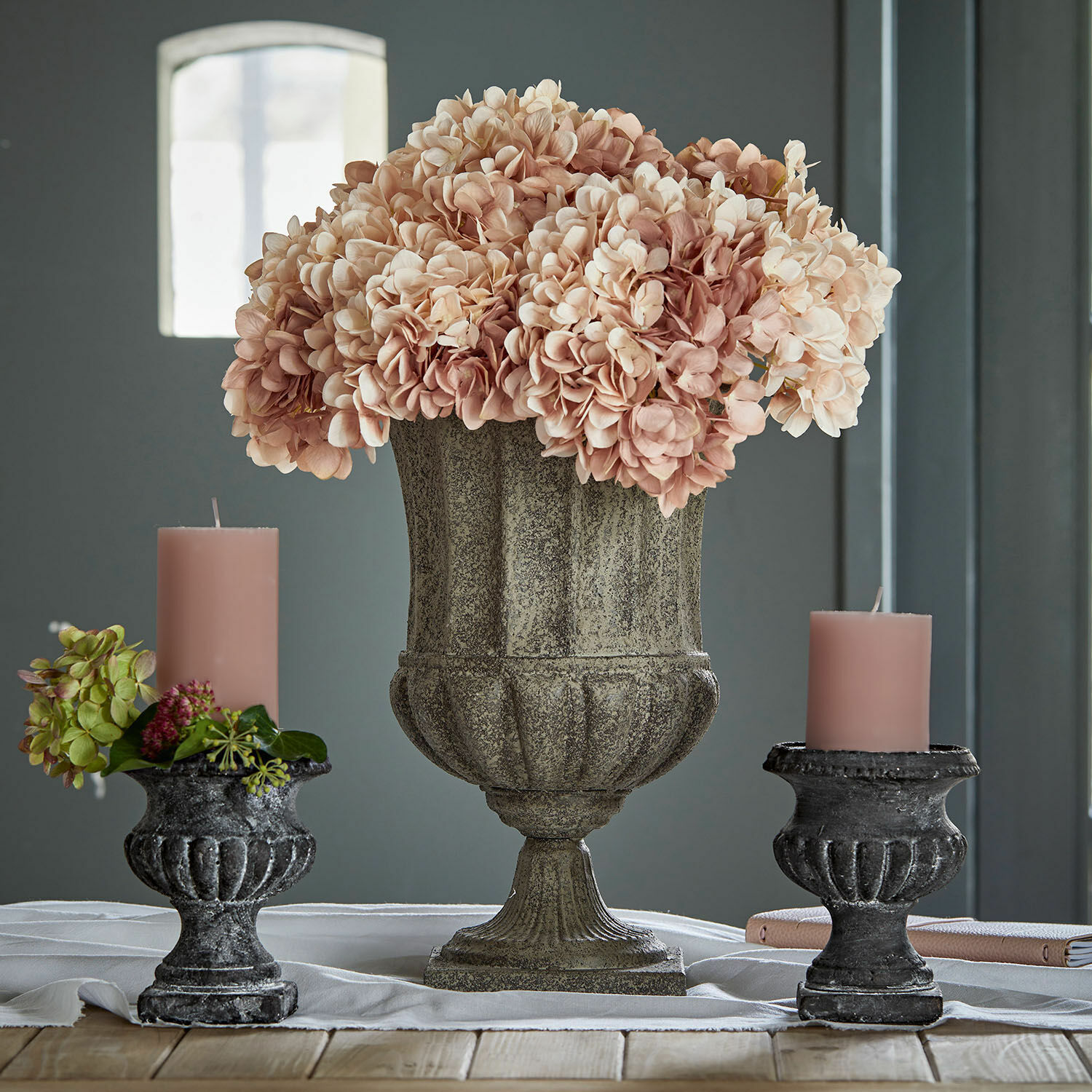 Amfoor Renny Decoratieve stenen vaas met roze bloemen en twee zwarte kandelaren met roze kaarsen op houten tafel