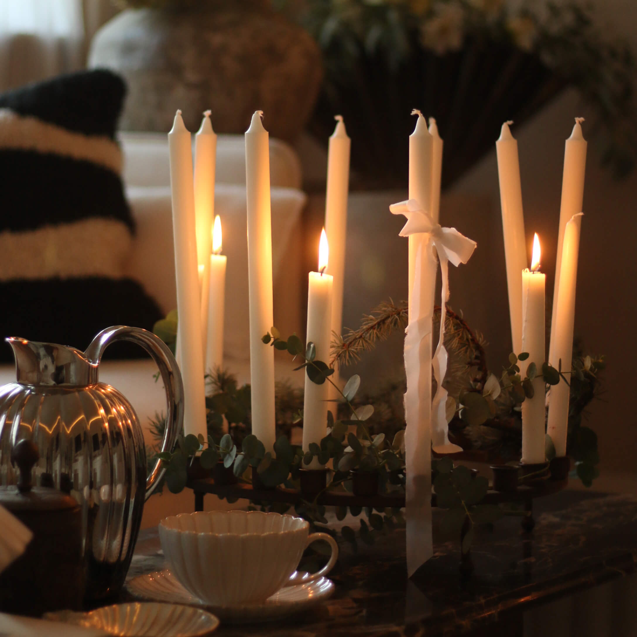Decoratieve kandelaar met witte kaarsen en groene bladeren op tafel in een gezellige kamer
