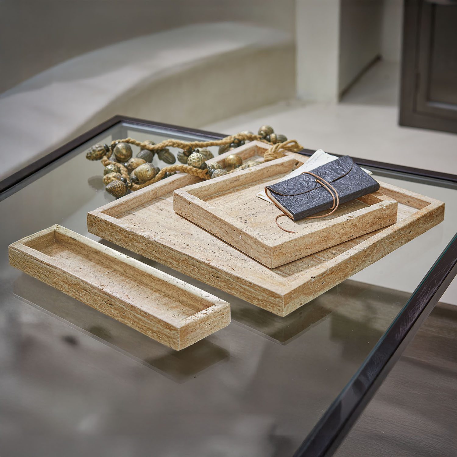 Set van drie rechthoekige beige stenen trays op een glazen tafel met zwarte rand