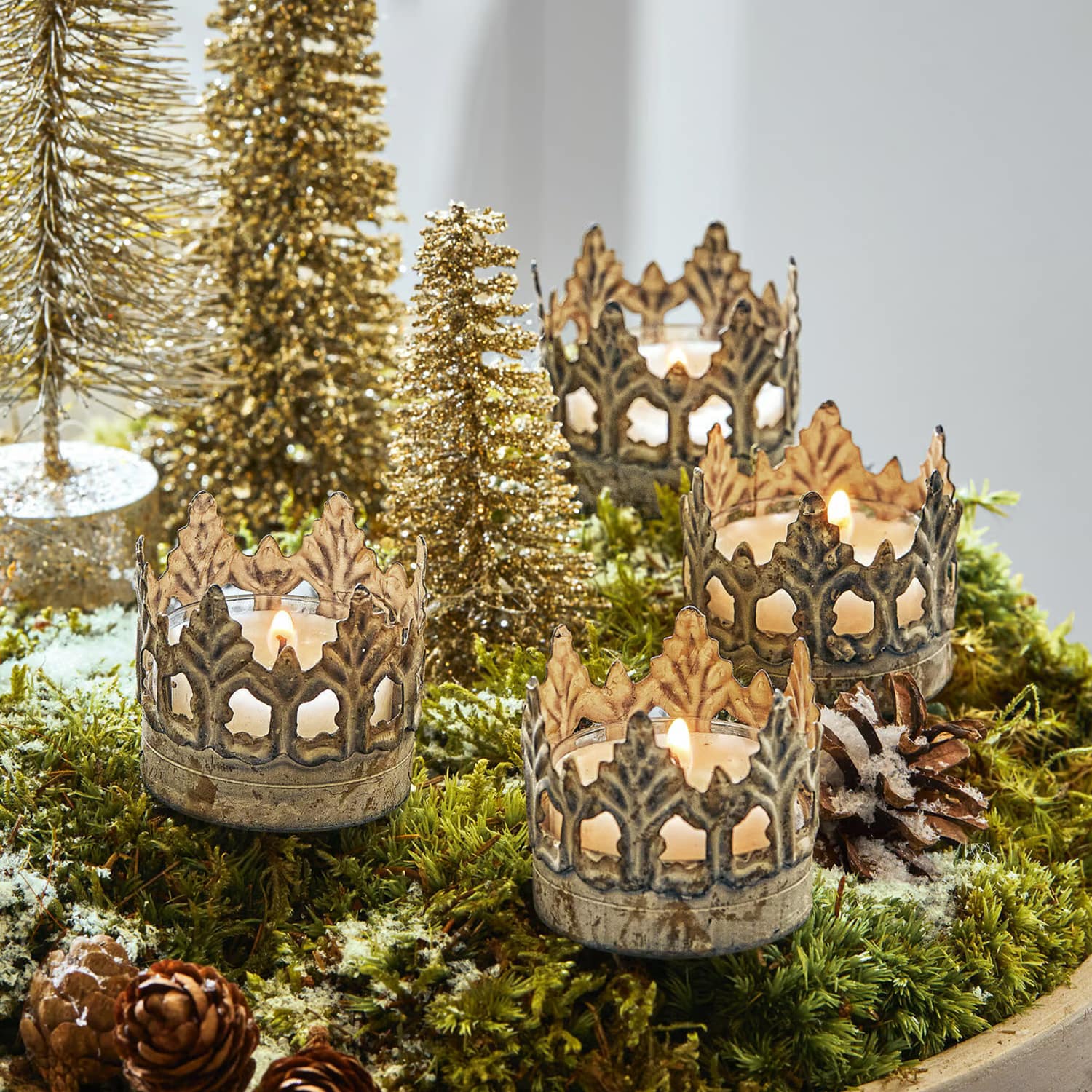 Metalen kandelaren in kroonvorm op groen mos met kerstdecoratie en gouden boompjes