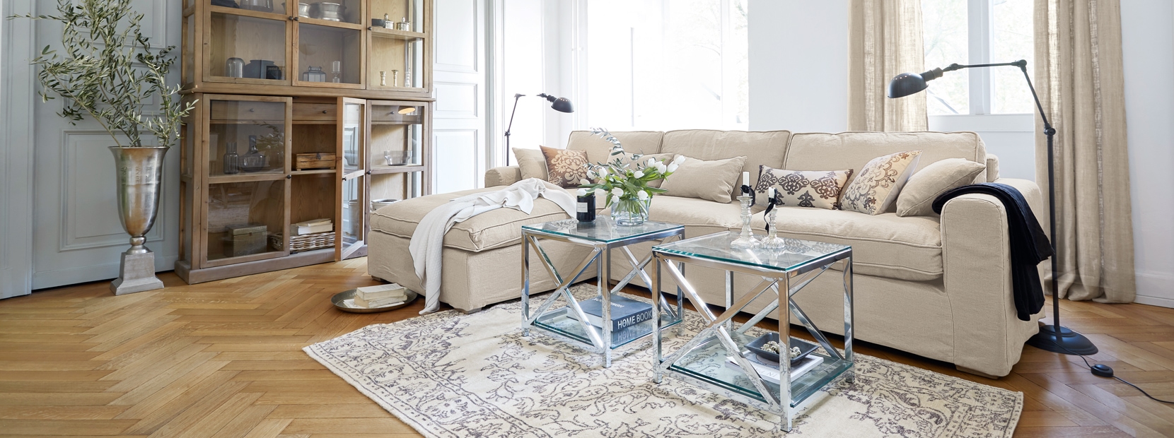 Klassiek elegante woonkamer met beige bank, glazen tafels en houten vitrinekast op lichte vloer