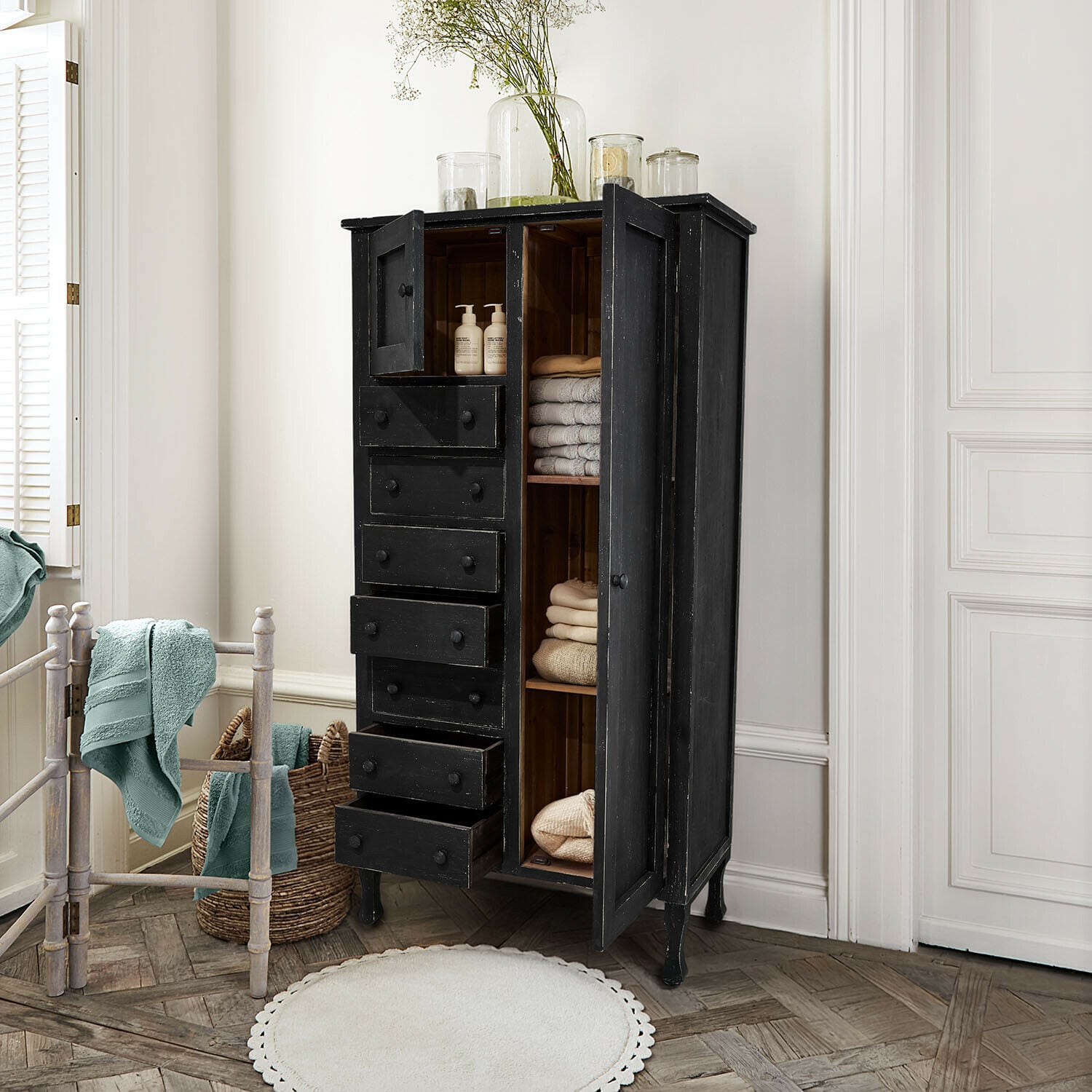 Zwarte houten kast met lades en planken, gevuld met handdoeken en verzorgingsproducten in badkamer