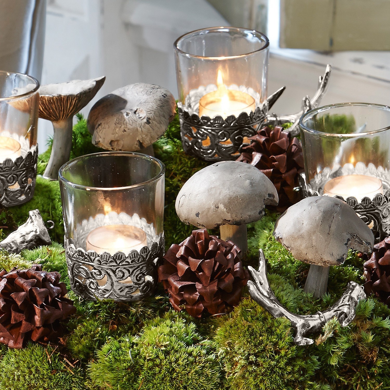 Tafeldecoratie met grijze paddenstoelen, glazen theelichthouders en groen mos voor feestelijke sfeer