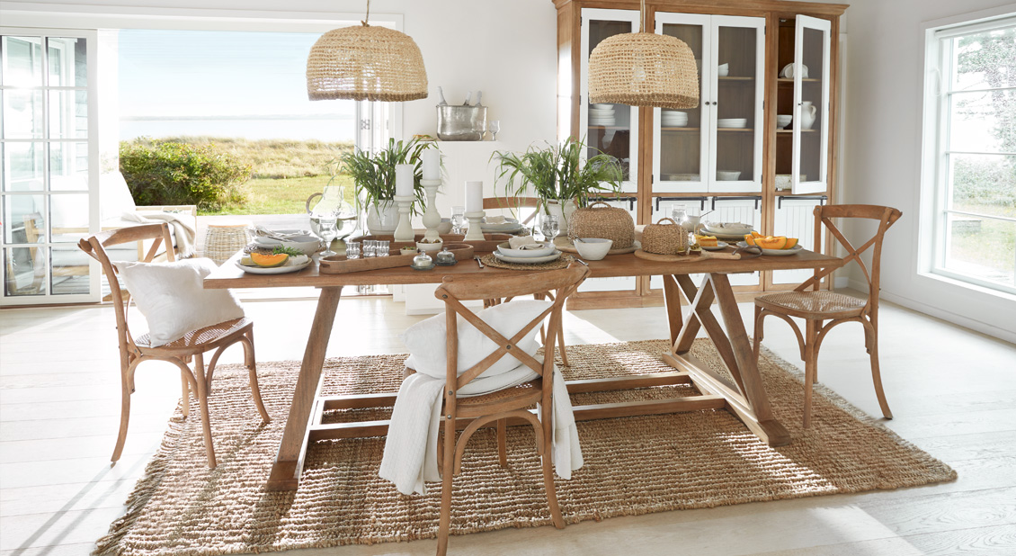 Eetkamer met houten tafel en rotan stoelen op natuurlijke vloerkleed, decoratie en uitzicht op tuin