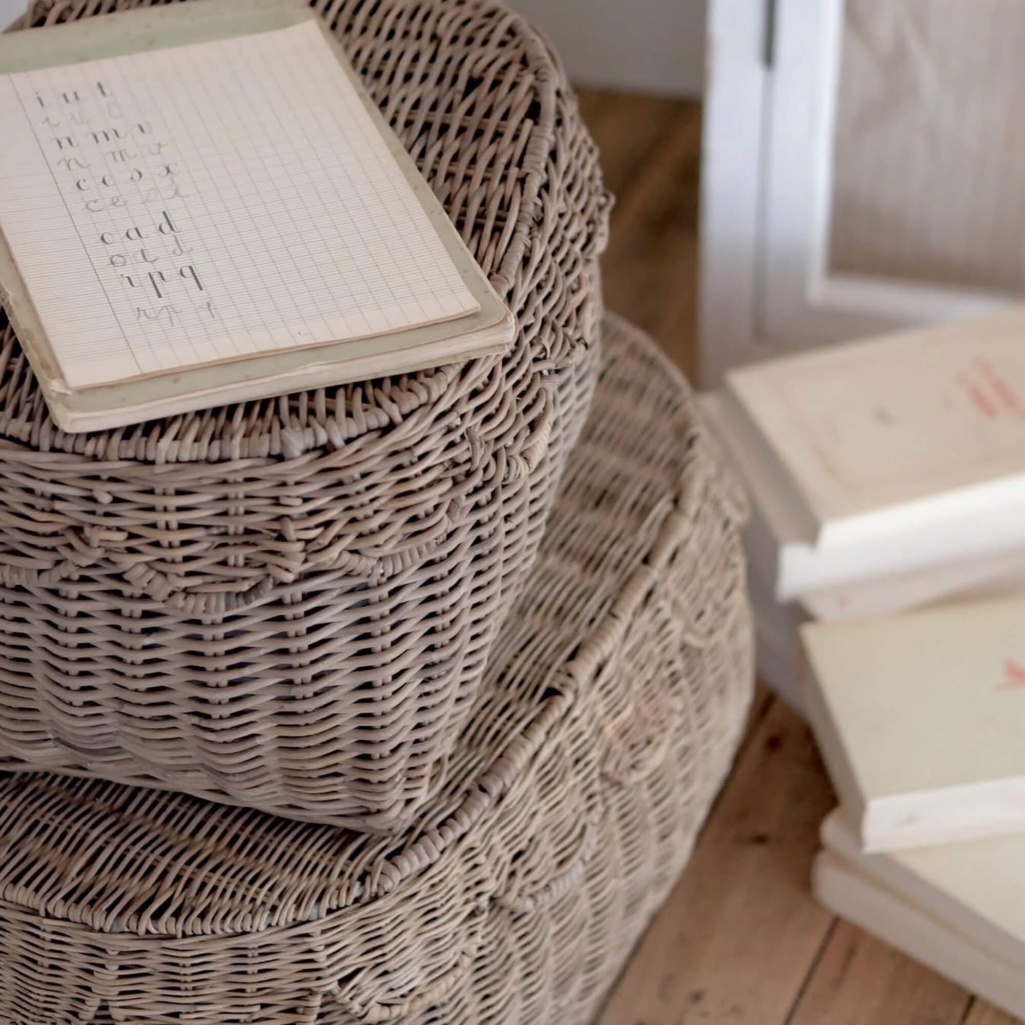 Beige gevlochten rieten manden gestapeld op houten vloer met notitieboekje erop