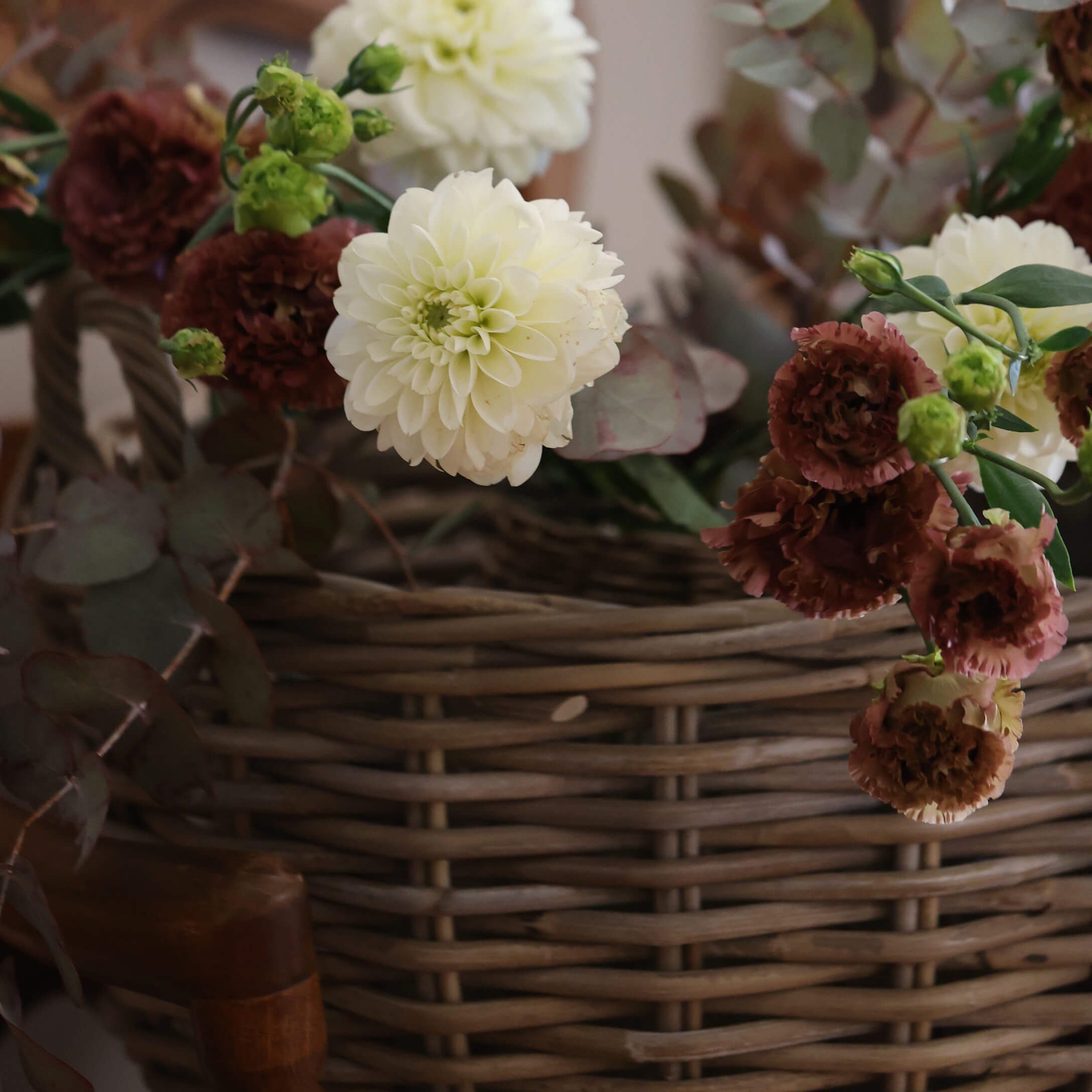 Boeket van crèmekleurige en bordeauxrode bloemen in een rieten mand voor interieurdecoratie