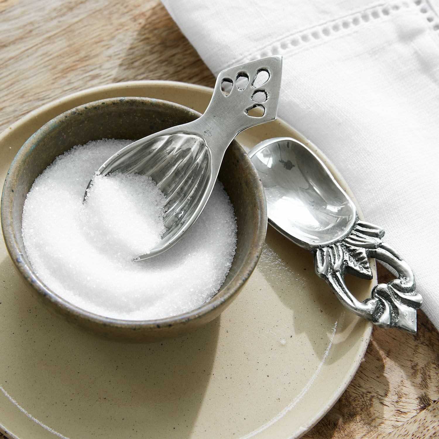 Zilverkleurige metalen suikerlepel met decoratief handvat in beige keramische kom met suiker