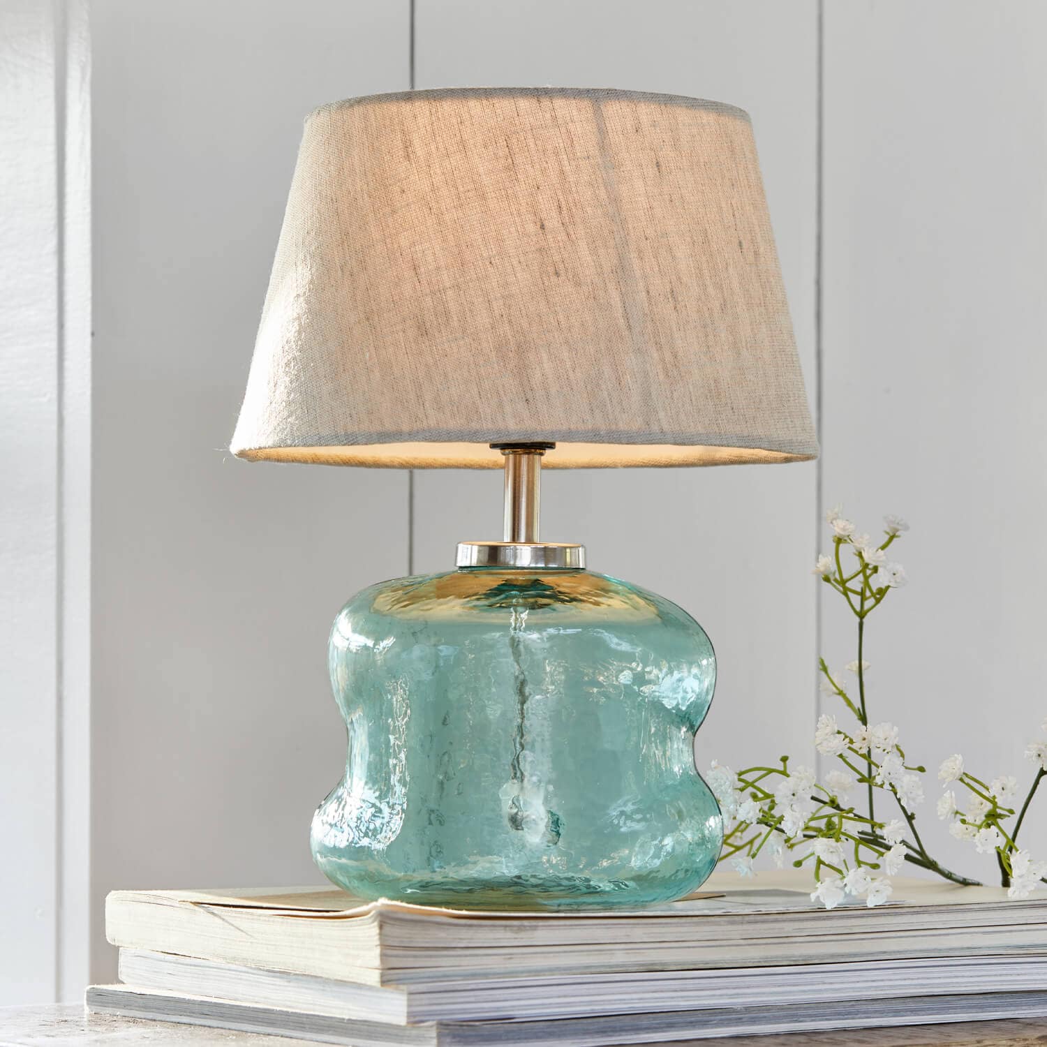 Tafellamp van blauw glas met beige kap op stapel boeken, interieurdecoratie