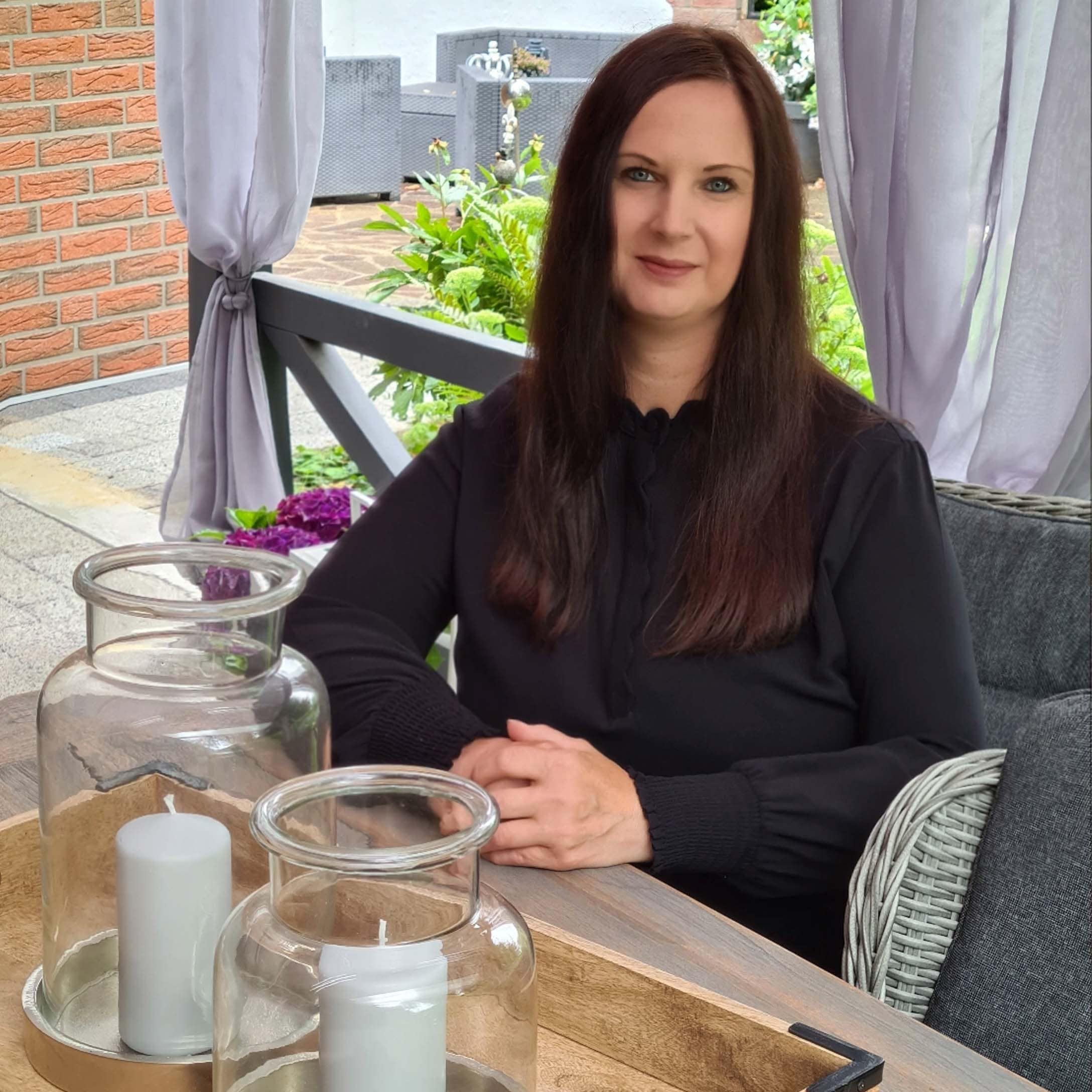 Vrouw in zwarte blouse zittend aan houten tafel met decoratieve kaarsen in glazen lantaarns