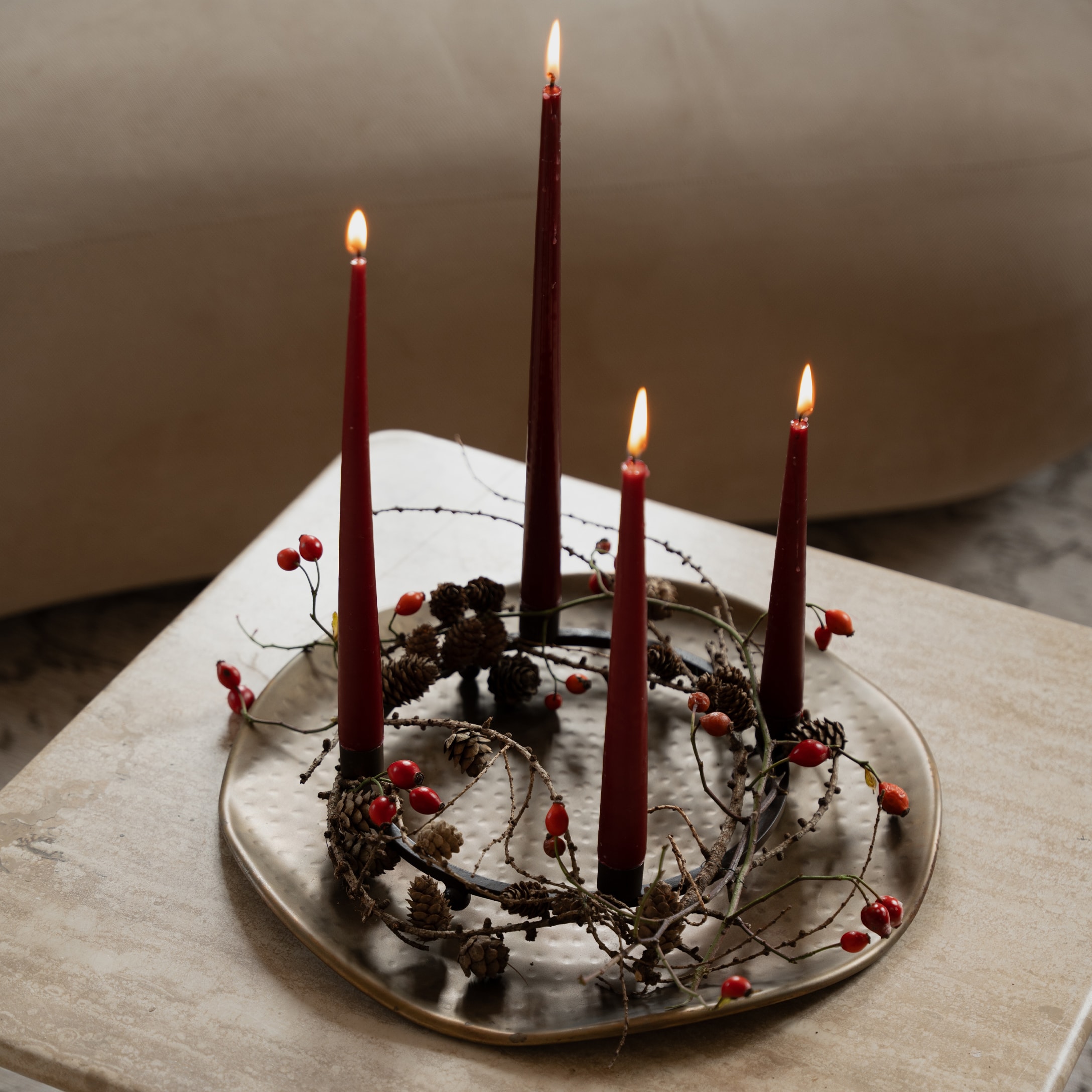 Adventskrans met rode kaarsen, dennenappels en rode bessen op metalen schaal