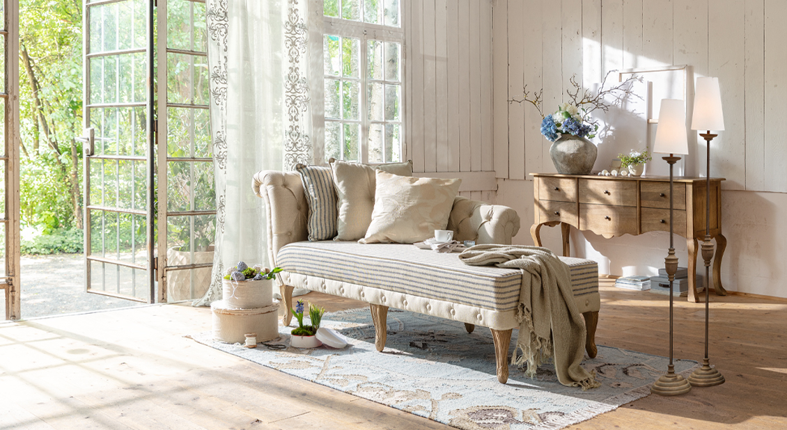 Beige gestoffeerde chaise longue met houten poten en kussens in lichte woonkamer met natuurlijk licht