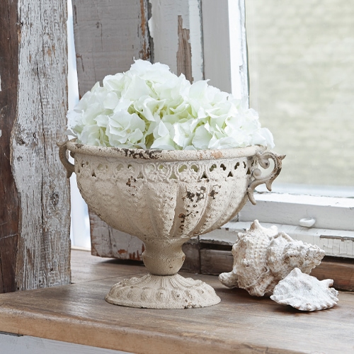 Decoratieve Vescemont amfoor van crèmekleurig metaal met witte bloemen op houten vensterbank