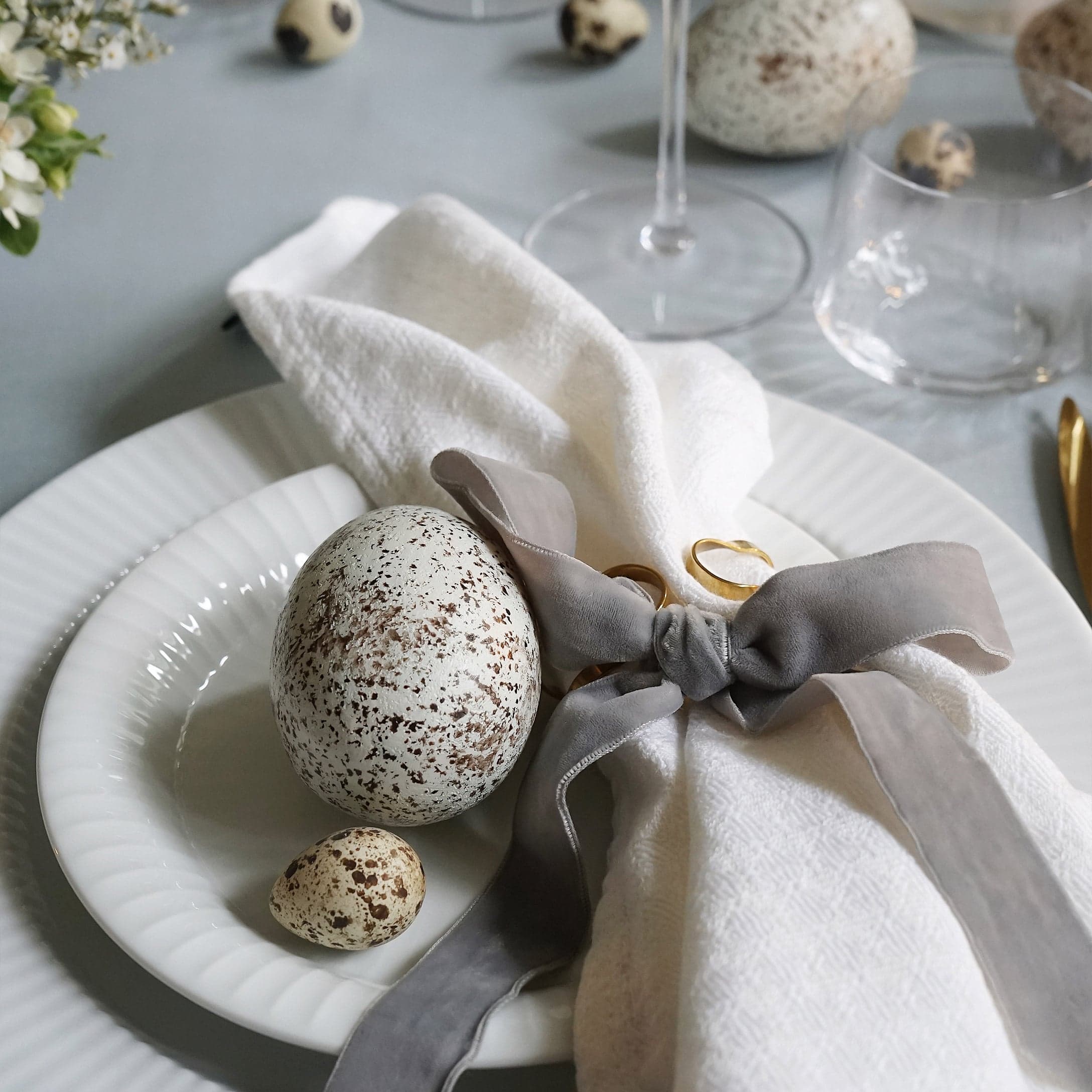 Witte borden met decoratieve gevlekte eieren en linnen servet met grijze strik op tafel