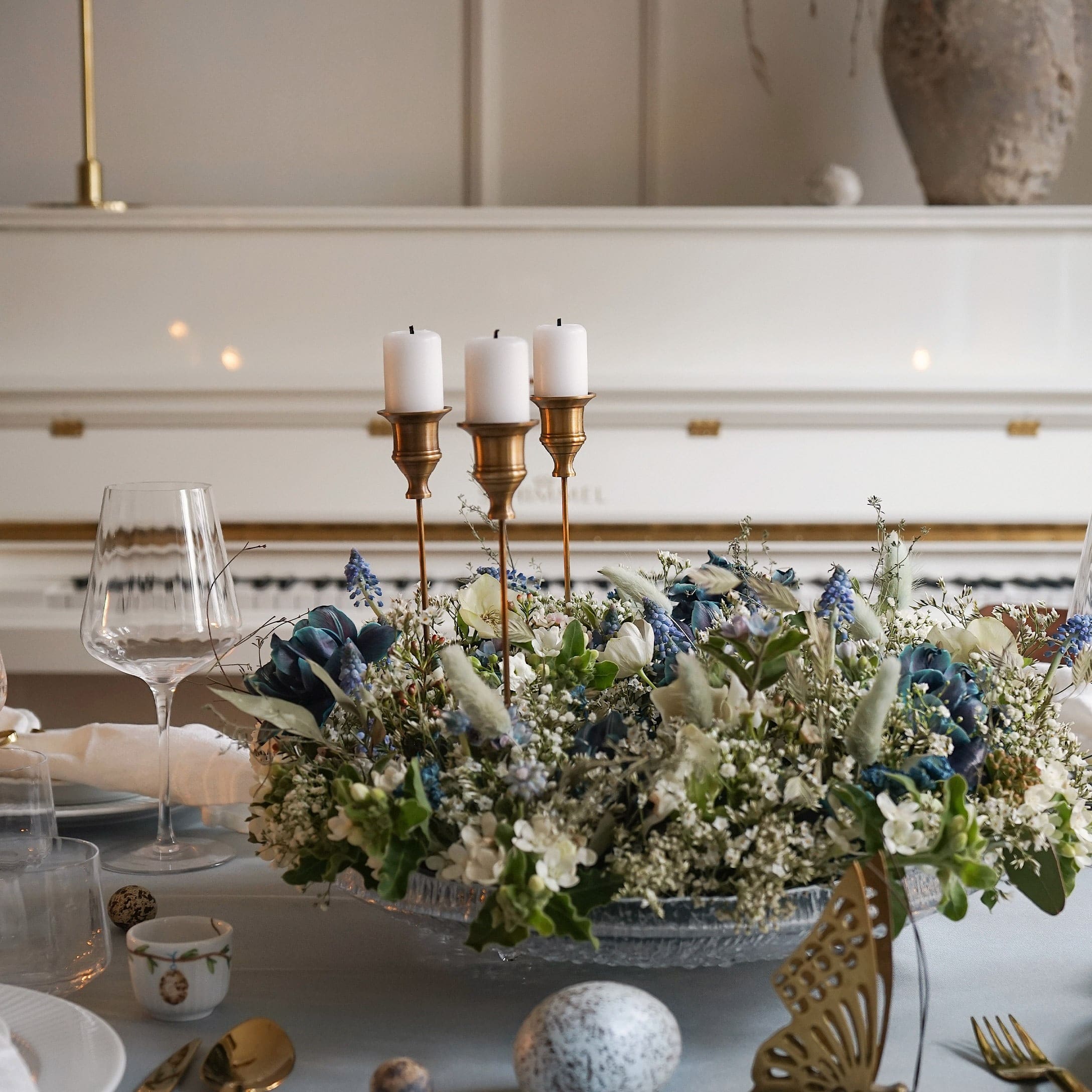 Decoratieve kandelaar met drie witte kaarsen en bloemstuk op glazen schaal