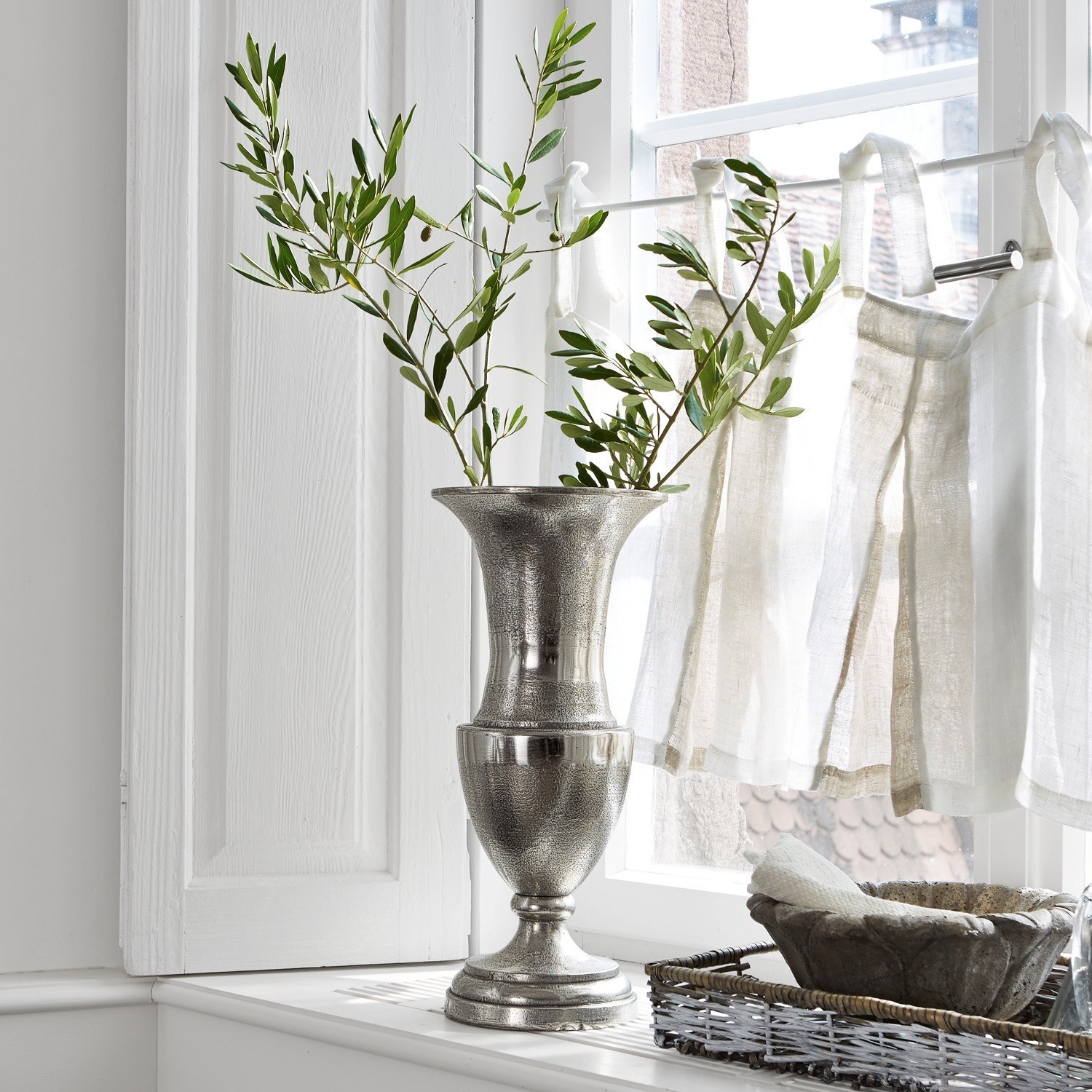 Zilveren metalen vaas op vensterbank met groene takken en natuurlijk licht