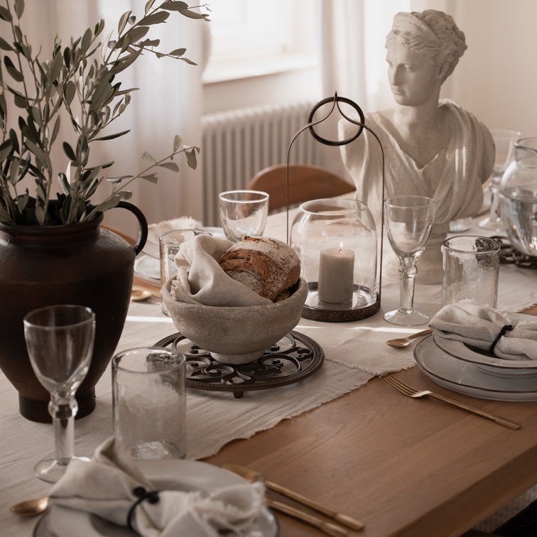 Rustieke tafel met stenen broodkom, kaars onder glazen stolp en witte stenen beeld als decoratie