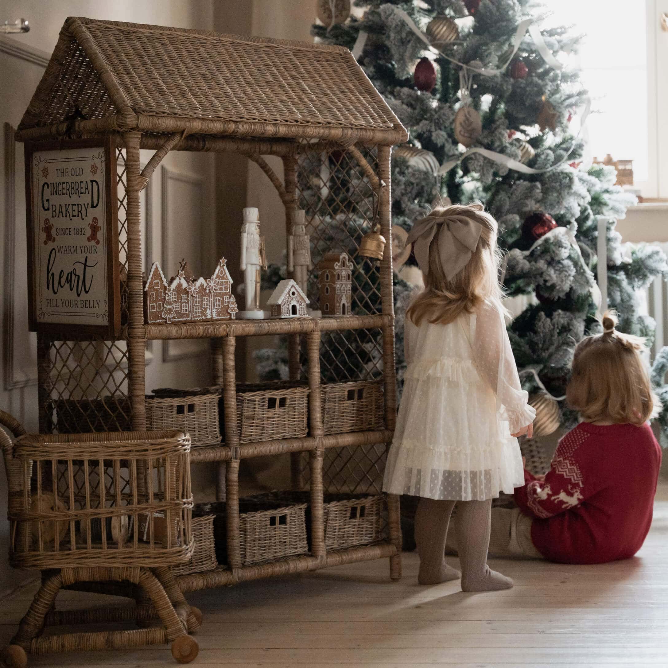 Rotan huis met peperkoekdecoraties naast kinderen bij versierde kerstboom in woonkamer