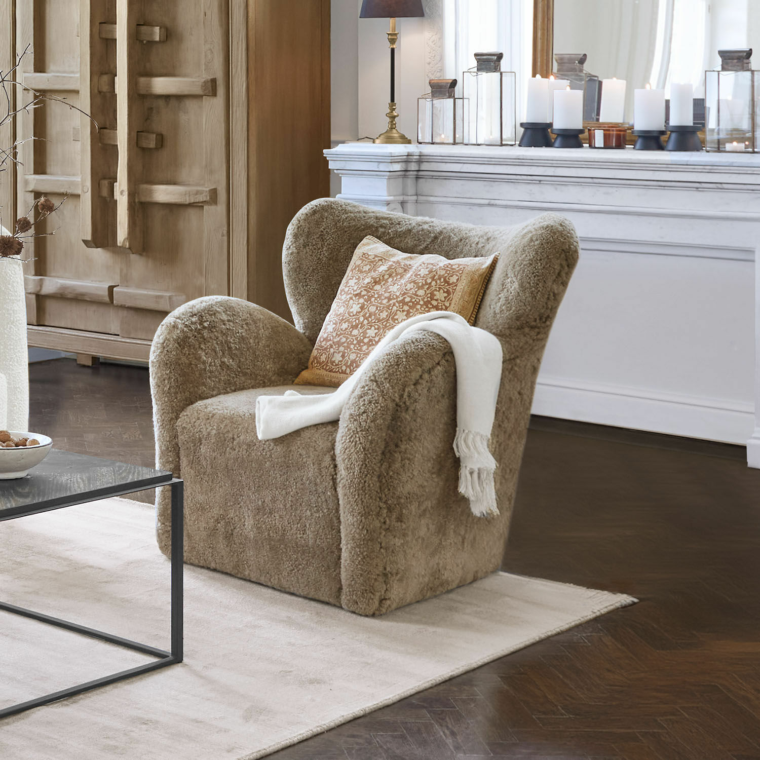 Fauteuil Ambrécourt Beige fauteuil van zachte stof met kussen en witte deken in elegante woonkamer