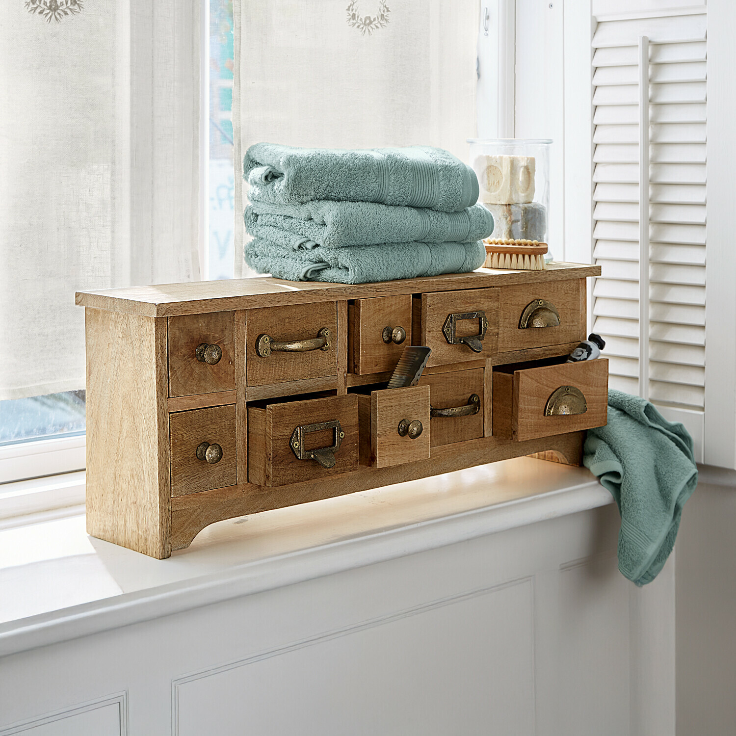 Houten kast met meerdere lades en zachte groene handdoeken op de vensterbank