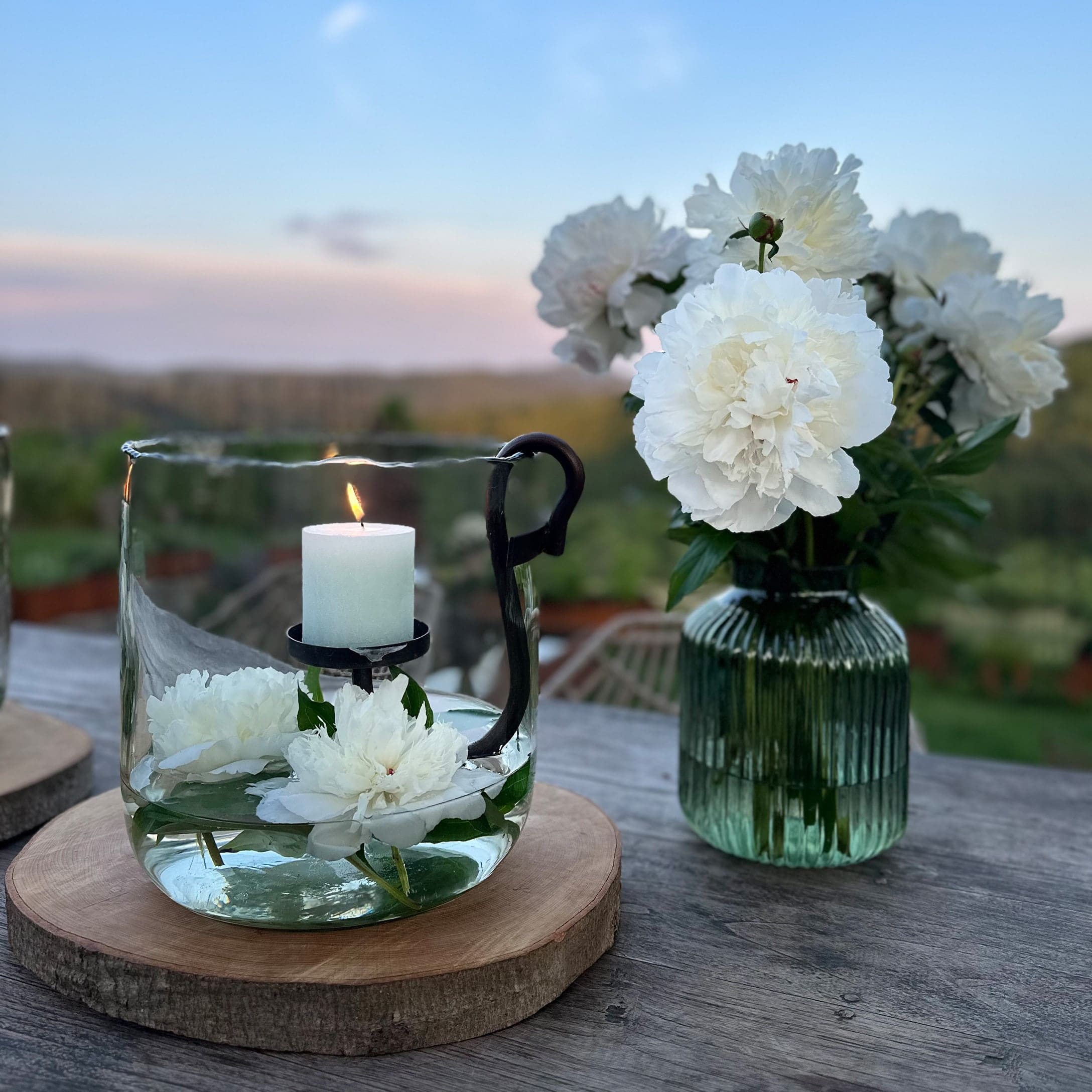 Glazen windlicht met witte kaars en witte bloemen op houten ondergrond buiten