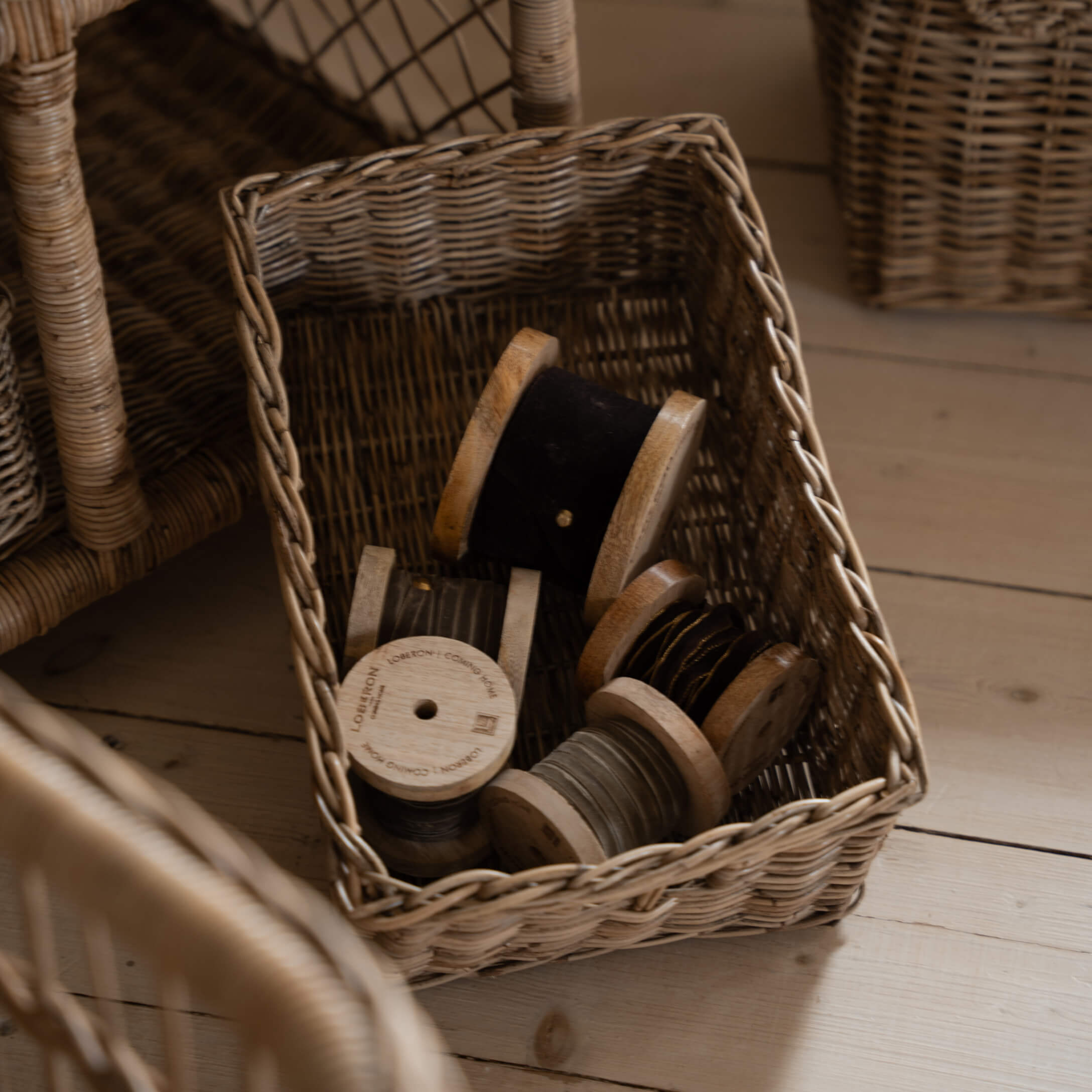 Rieten mand met houten spoelen met zwarte en grijze draad op lichte houten vloer