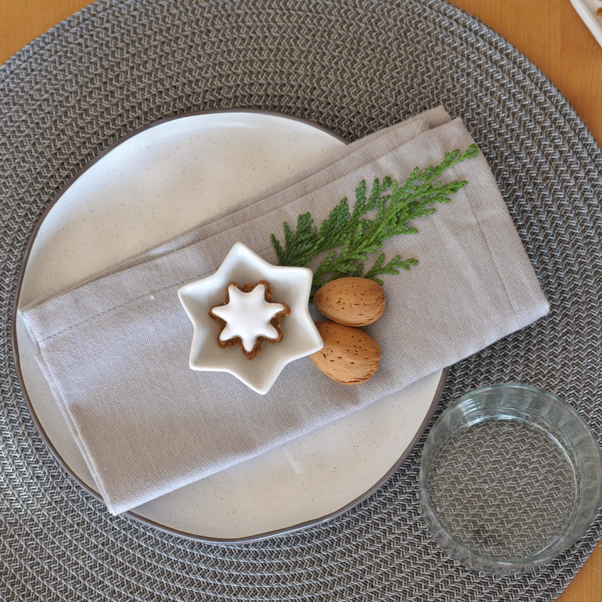 Grijze gevlochten placemat met wit bord, linnen servet en kerstdecoratie