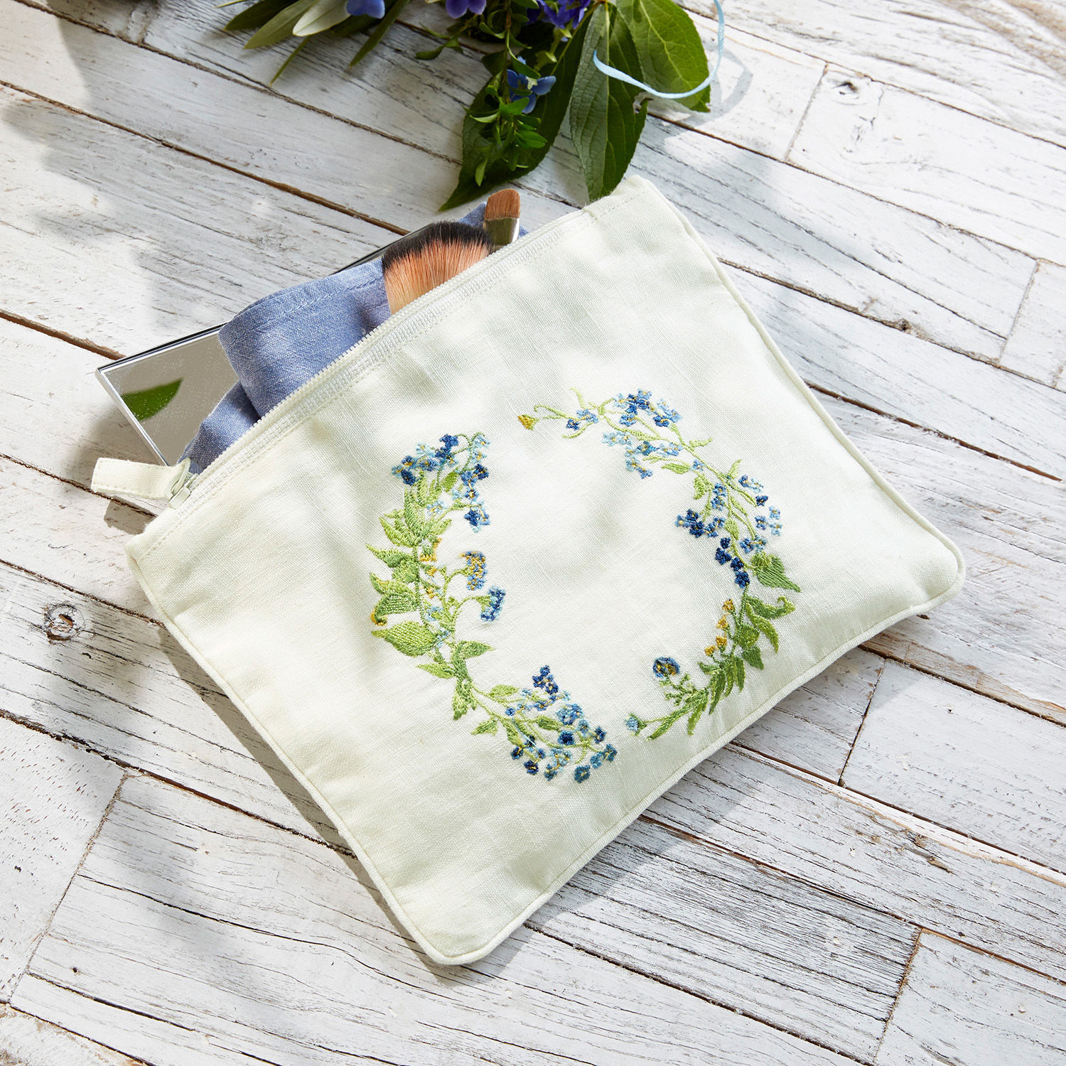 Witte linnen make-uptas met blauwe bloemenborduursel op lichte houten achtergrond