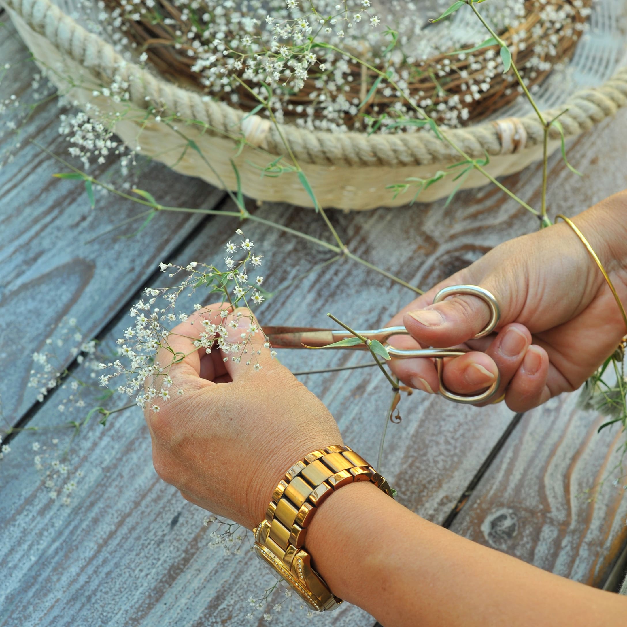 Handen knippen fijne witte bloemen op houten tafel met herfstdecoratie in mand