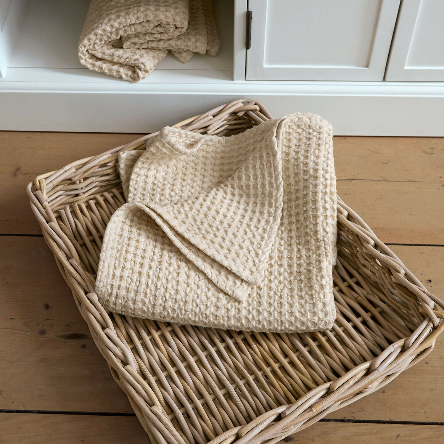 Handdoek Maralei Beige katoenen wafelplaid in een rieten mand op een lichte houten vloer