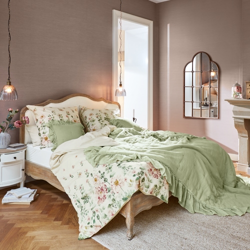 Slaapkamer met houten bed, groene en bloemige beddengoed, hanglamp en decoratieve spiegel aan de muur