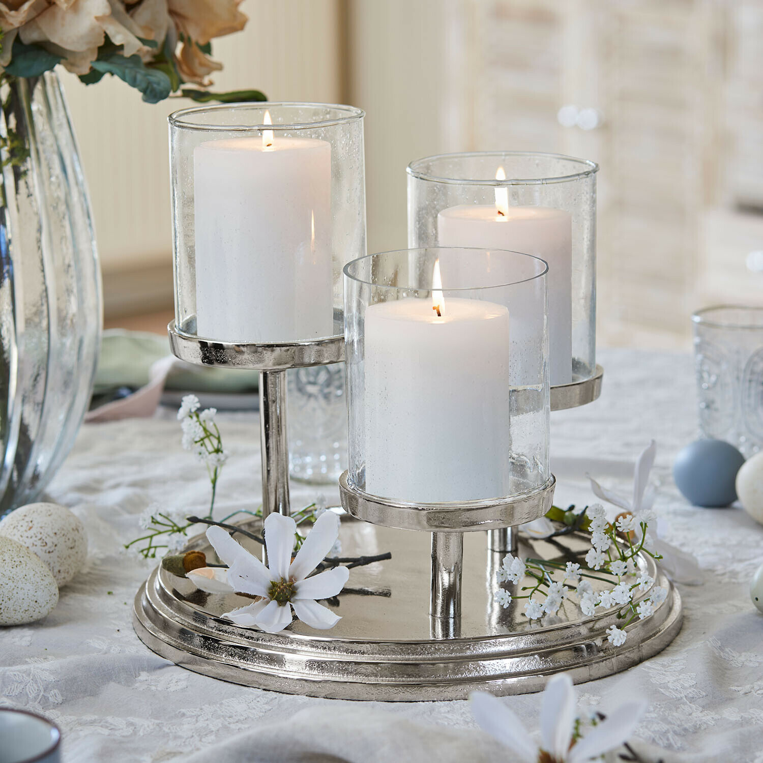Driedelige metalen kandelaar met witte kaarsen en glazen kappen als tafeldecoratie